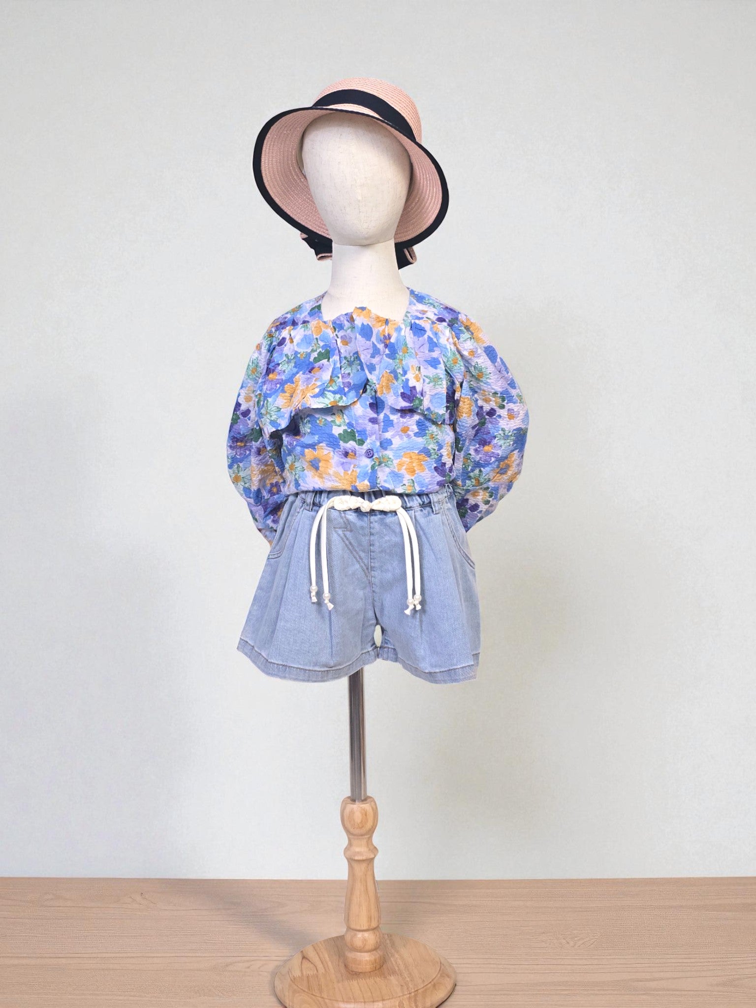 Kids clothing Mannequin wearing a floral blouse and denim shorts with a hat on a white background. Blue