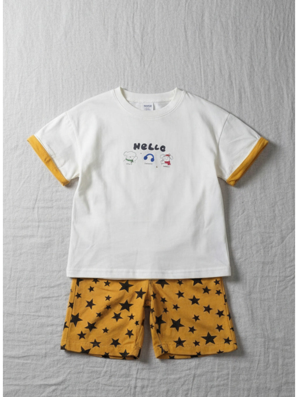 White t-shirt with yellow trim and star-patterned shorts on a textured gray surface