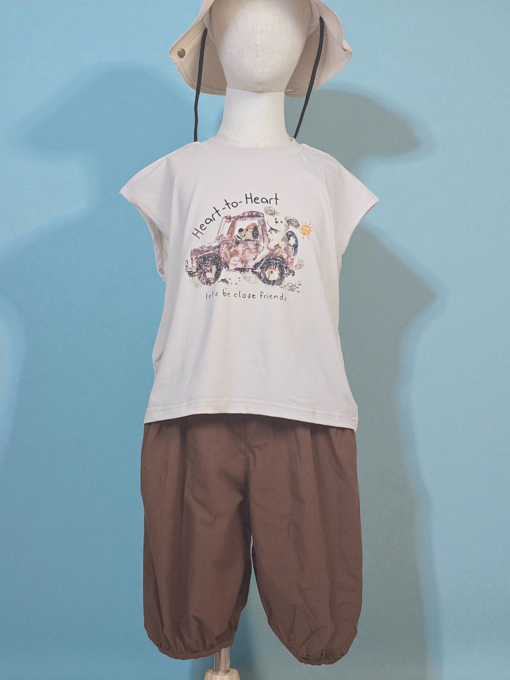 Mannequin wearing a white t-shirt with a graphic design and brown pants against a light blue background