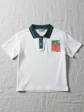 Children's white short-sleeve polo shirt featuring a dark teal contrast collar and placket with a colorful block graphic on the chest.