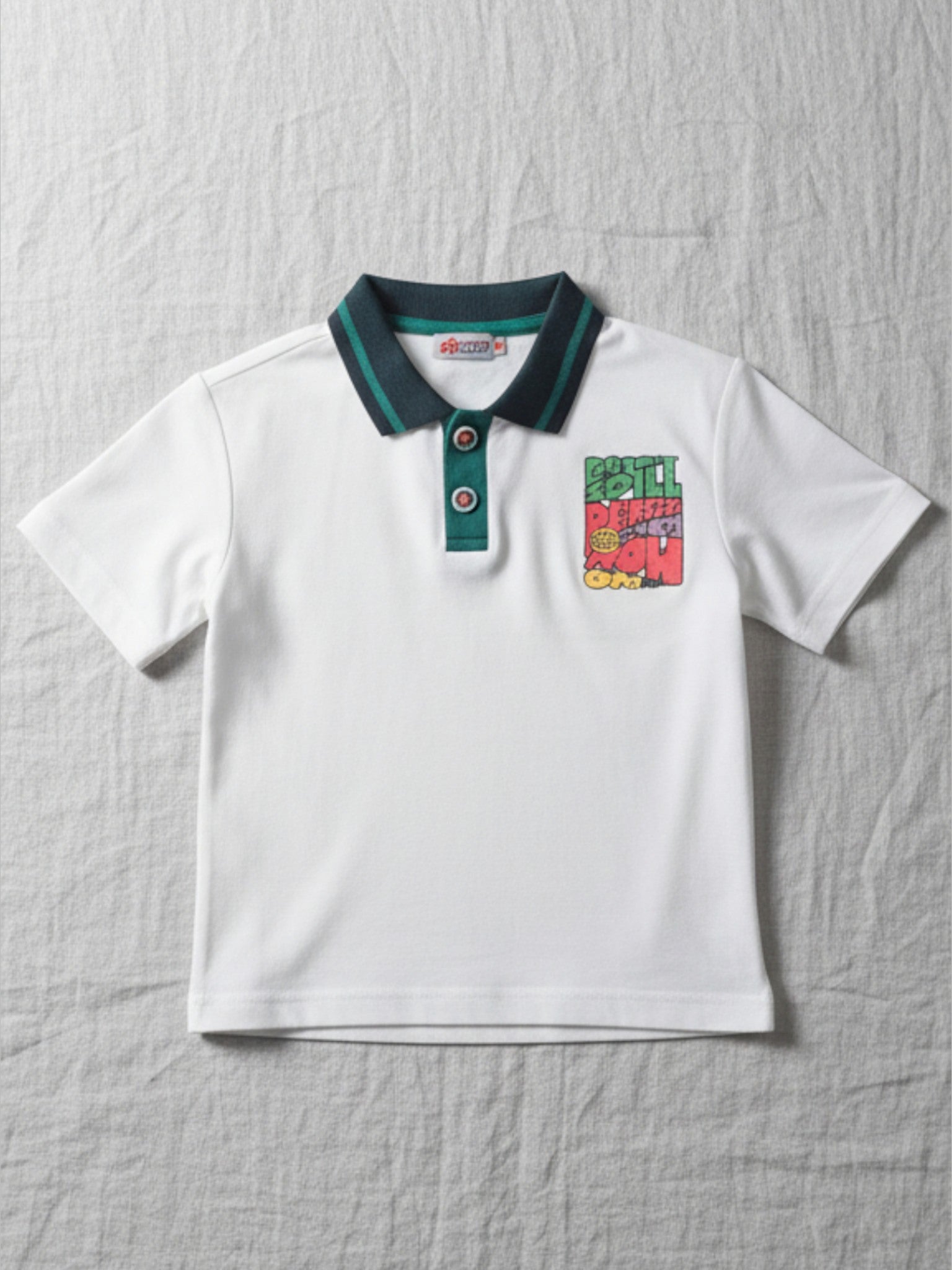 Children's white short-sleeve polo shirt featuring a dark teal contrast collar and placket with a colorful block graphic on the chest.