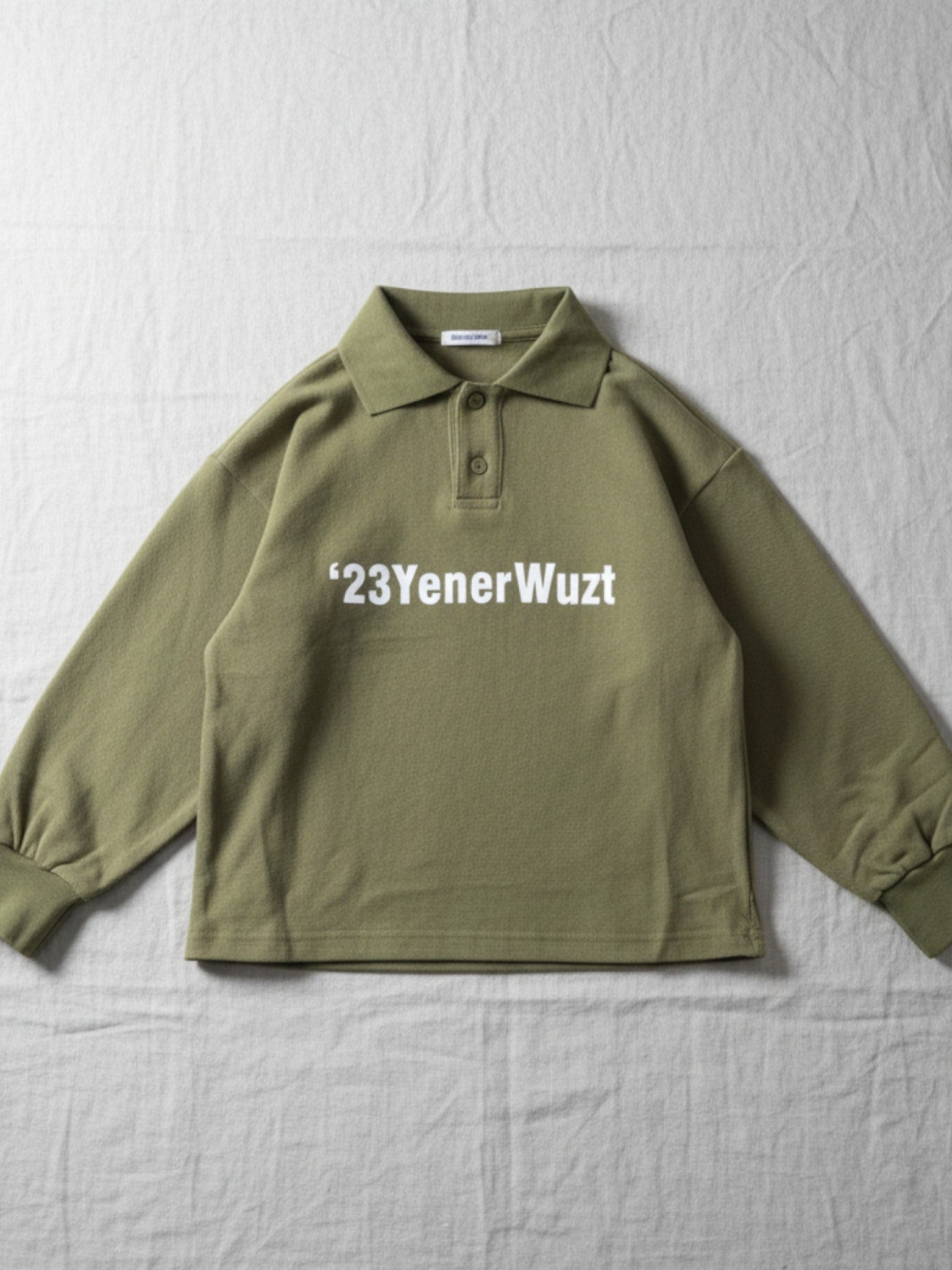 Children's olive green long-sleeve polo shirt featuring a classic collar, two-button placket, and white "'23YenerWuzt" text graphic on the chest