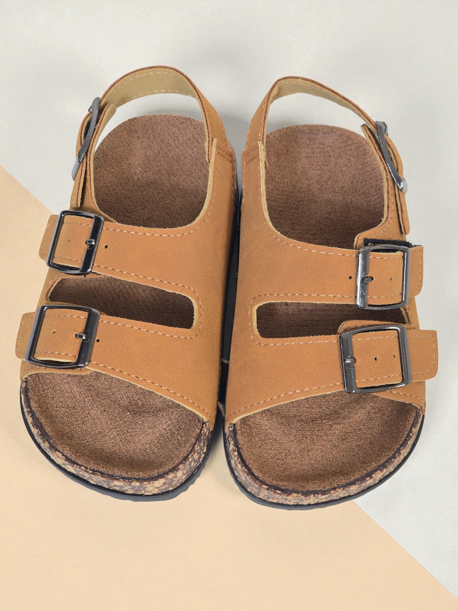 Pair of Kids Birkenstock style brown sandals with buckles on a light surface. Brown