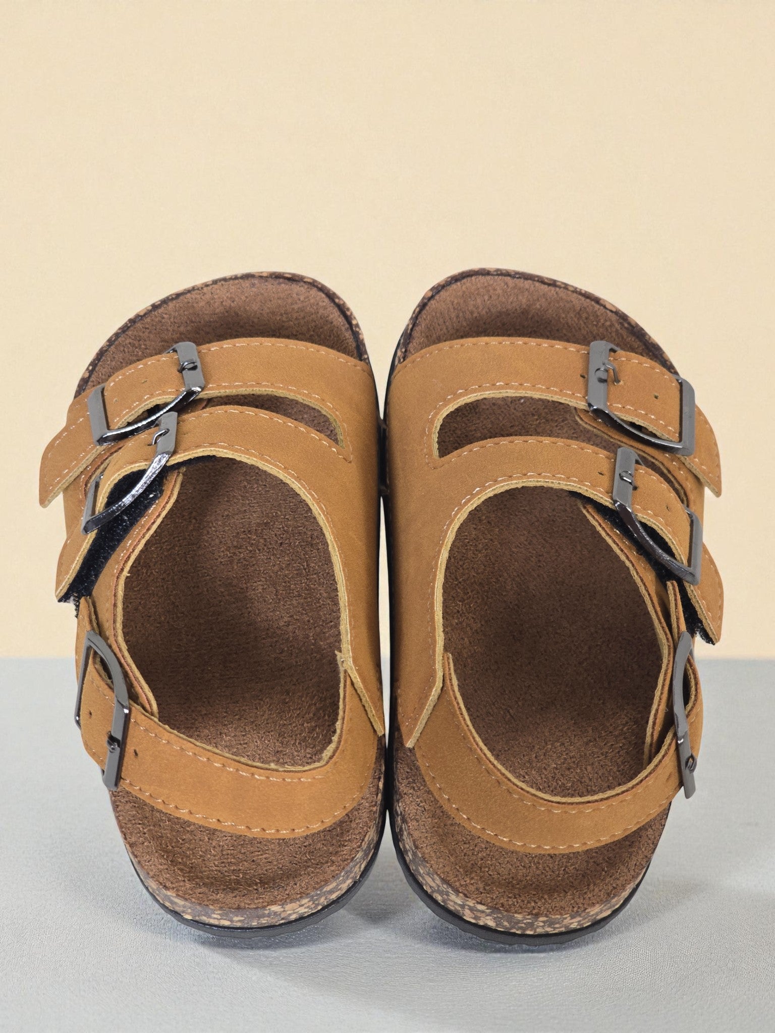 Pair of Kids Birkenstock style brown sandals with buckles on a light surface. Brown