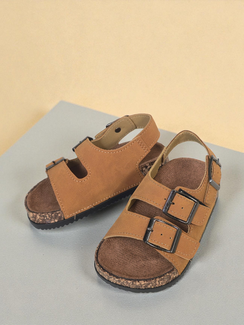 Pair of Kids Birkenstock style brown sandals with buckles on a light surface. Brown