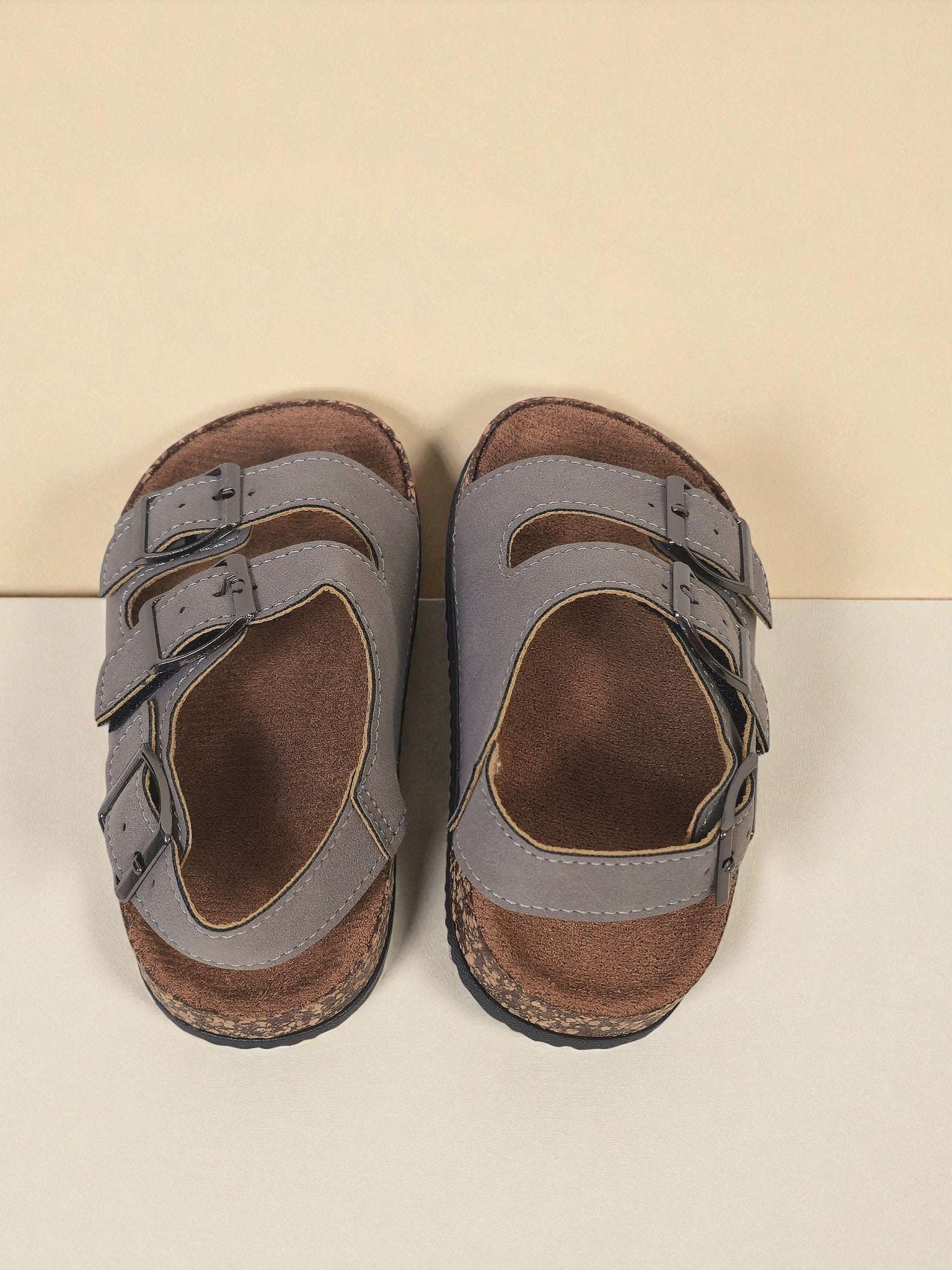 Pair of Kids Birkenstock style sandals with buckles on a light gray surface. Gray