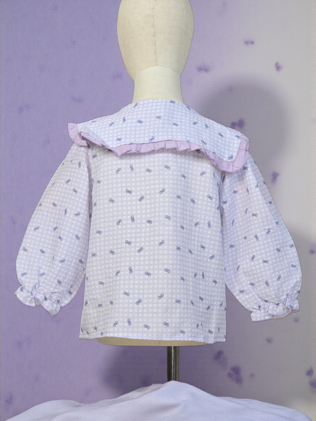 White blouse with ruffled collar on a mannequin against a purple background. Lilac