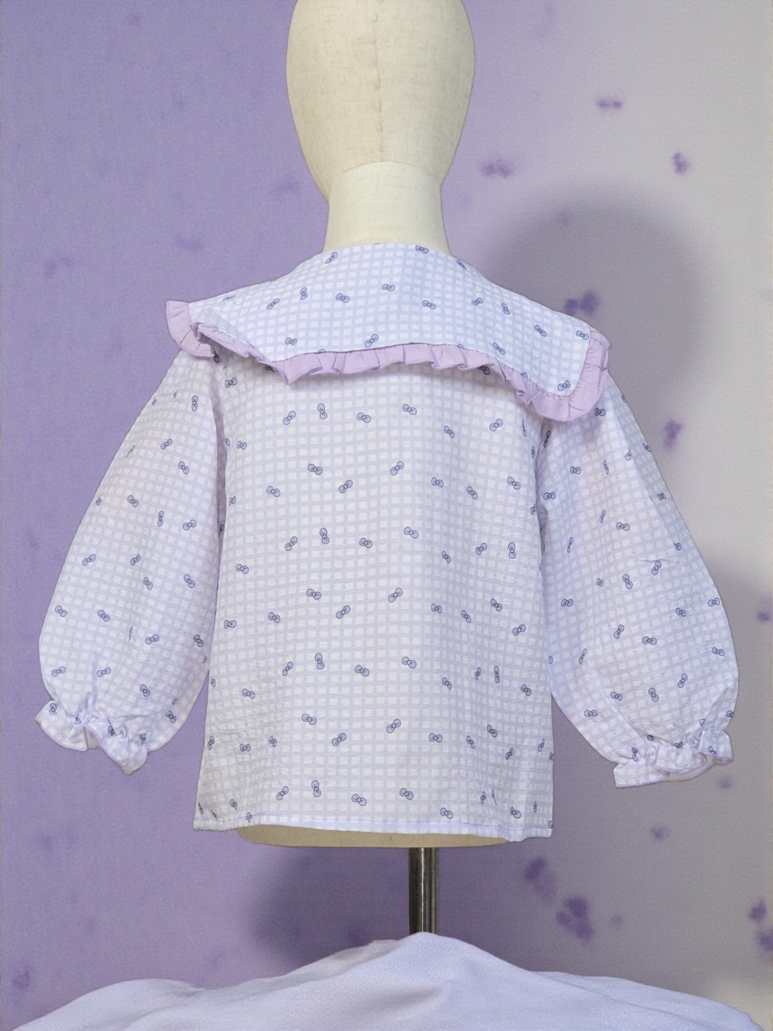White blouse with ruffled collar on a mannequin against a purple background. Lilac