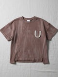 Children's short-sleeve t-shirt in a faded, washed brown finish featuring a white contrast pocket with a brown letter "U" and side slits at the hem.