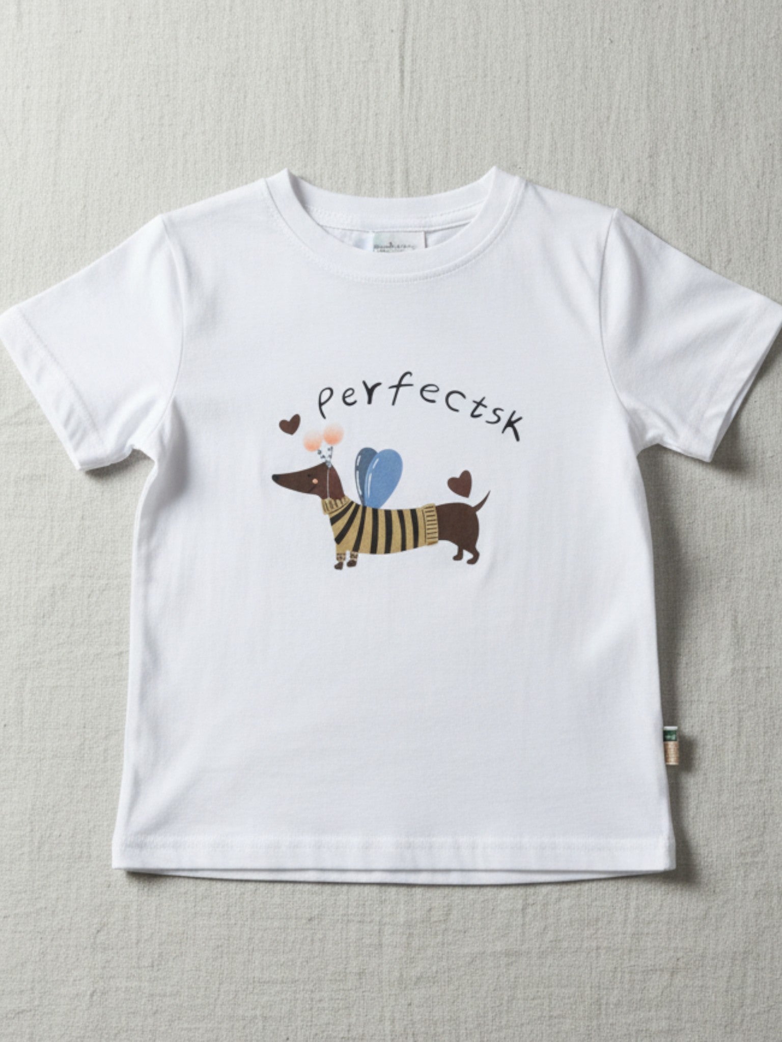 Children's white short-sleeve t-shirt featuring a central illustration of a dachshund wearing a striped sweater and blue wings with the text "perfectsk" above.