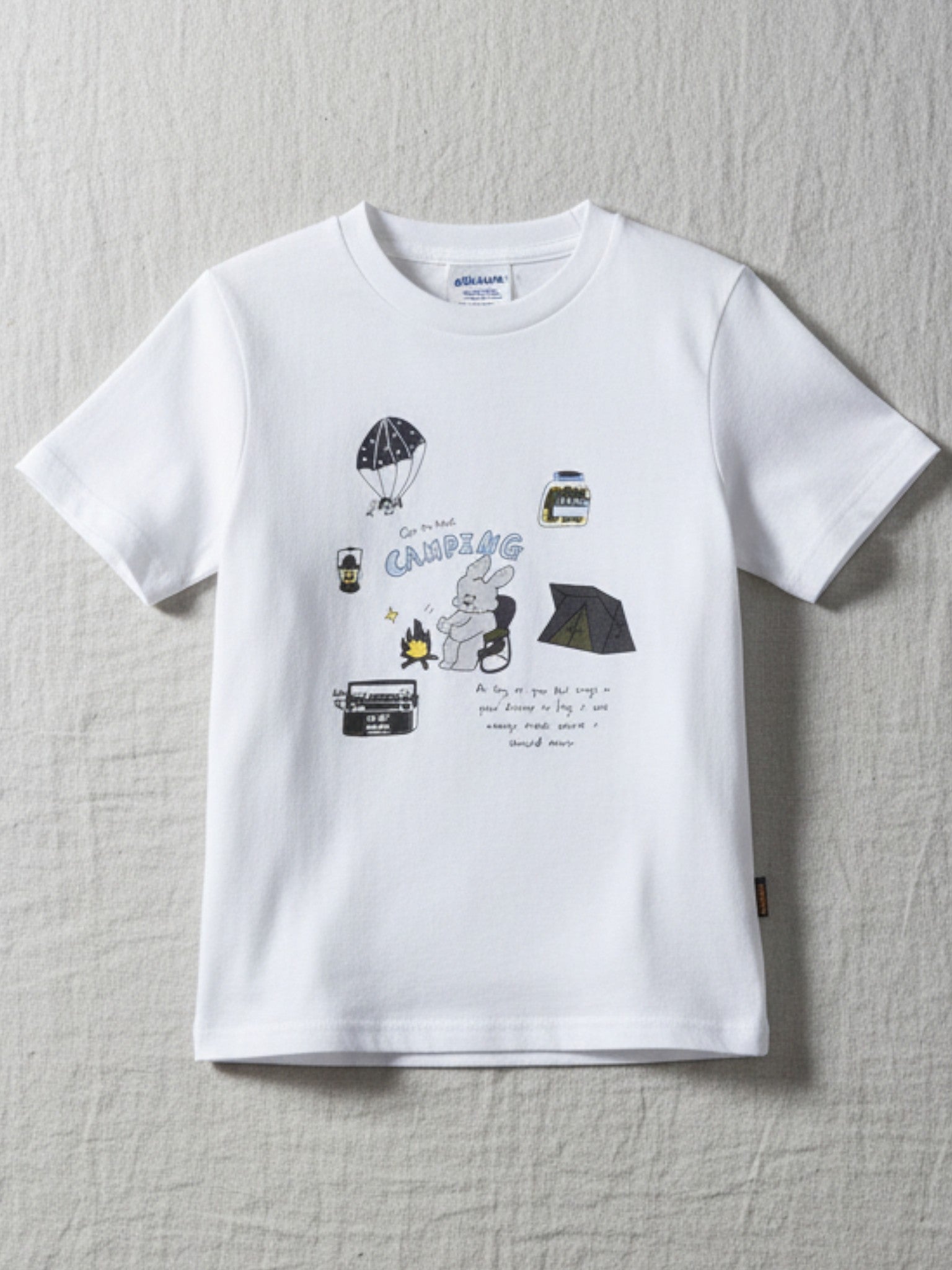 Children's white short-sleeve t-shirt featuring a playful "Camping" themed illustration with a bunny by a campfire, a tent, and a parachute.