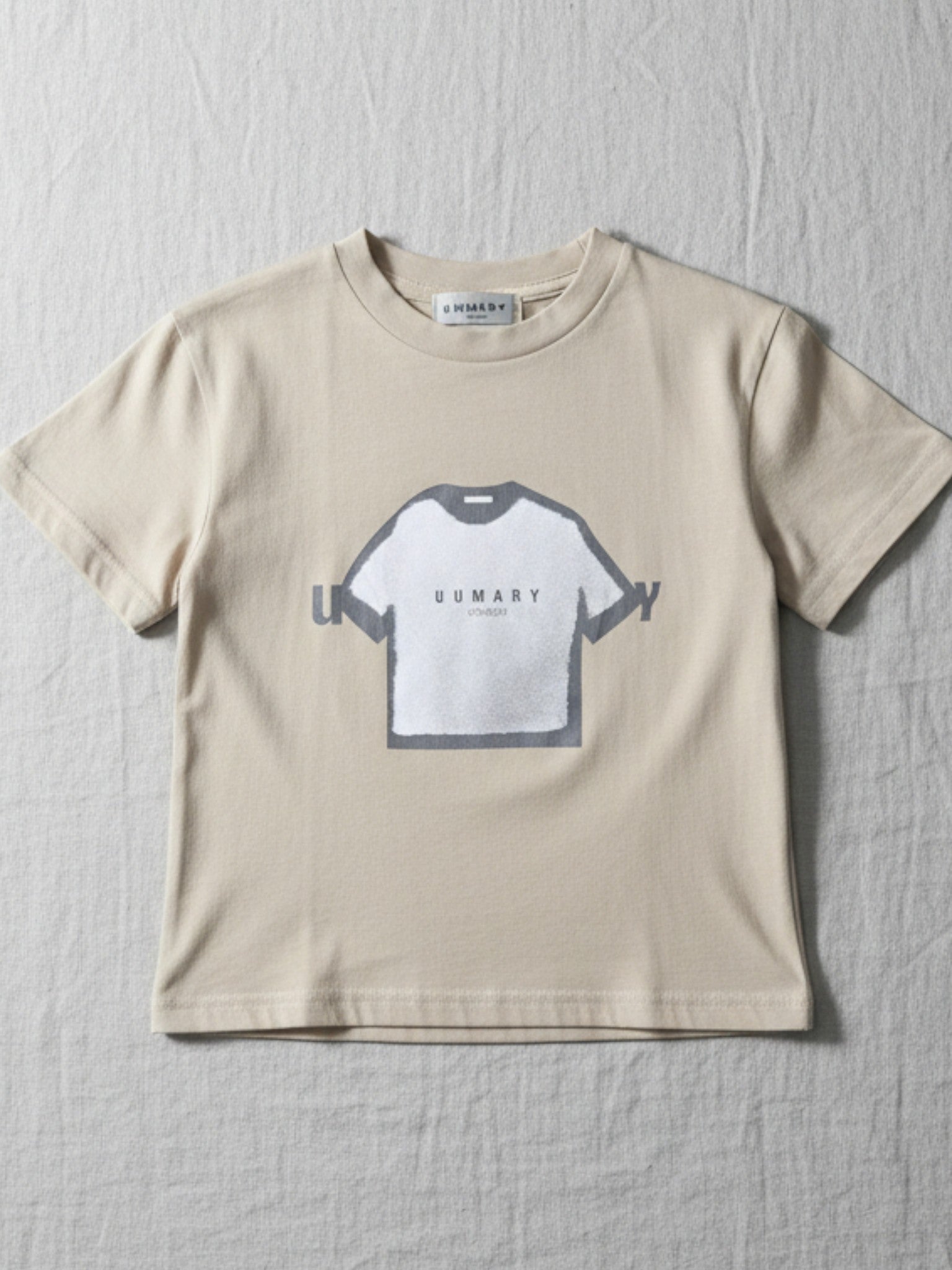 Children's short-sleeve t-shirt in a warm beige tone, featuring a central grey and white graphic of a t-shirt with "UUMARY" text.