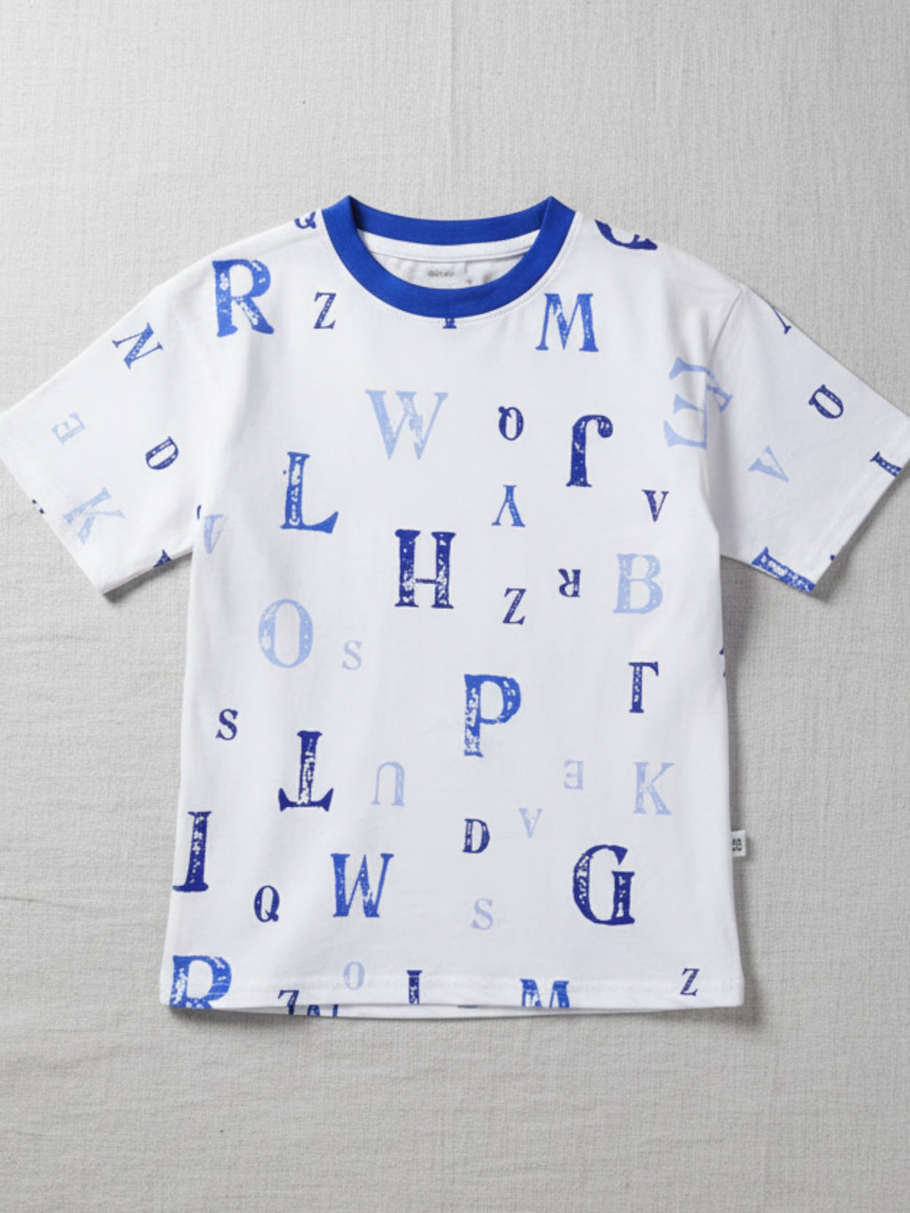 Children's white short-sleeve t-shirt with a blue crew neck, featuring a scattered print of various alphabet letters in shades of blue.