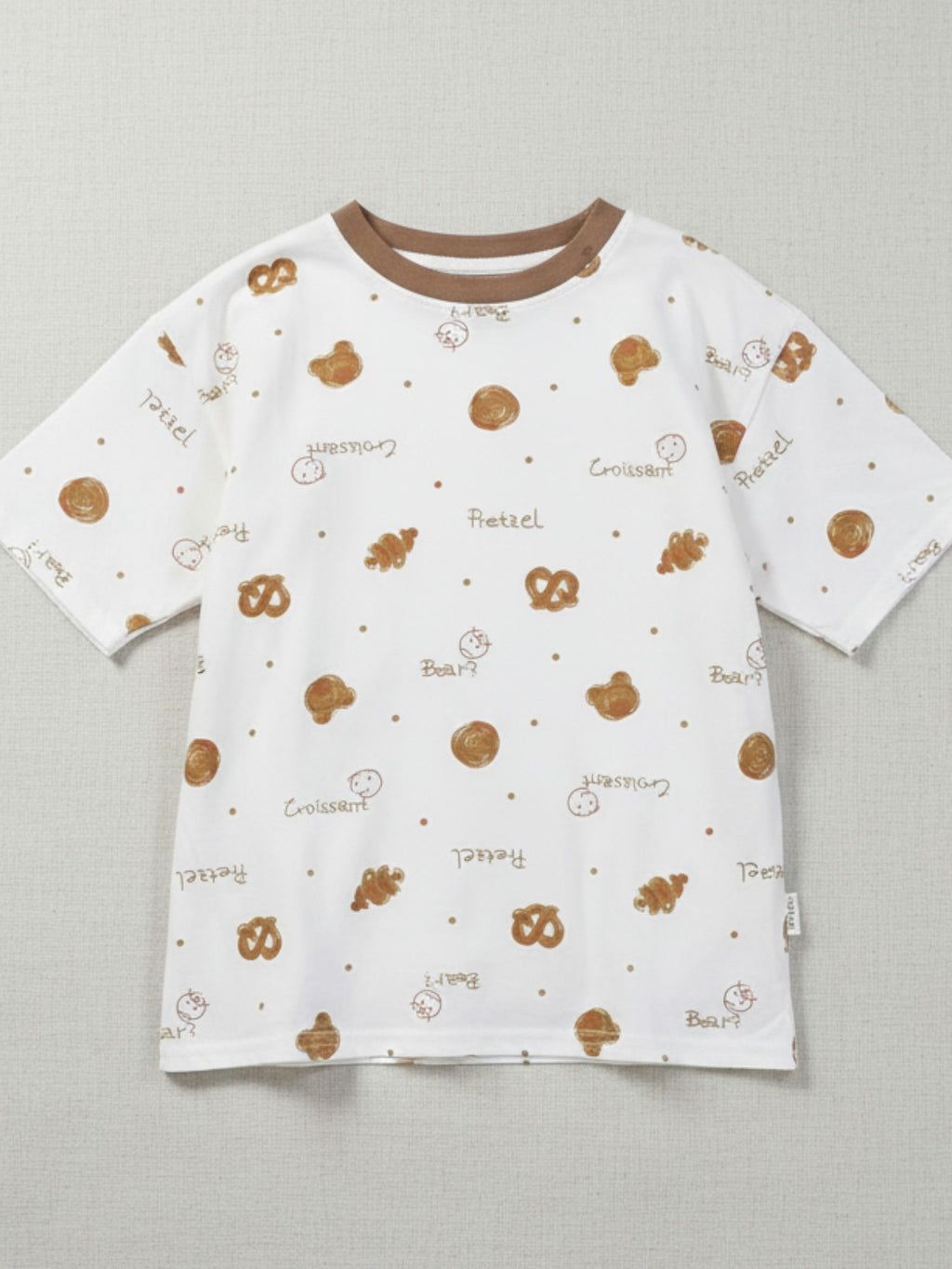 Children's white short-sleeve t-shirt with a brown crew neck, featuring a tossed print of pretzels, croissants, and bear faces with "Pretzel" and "Croissant" text.