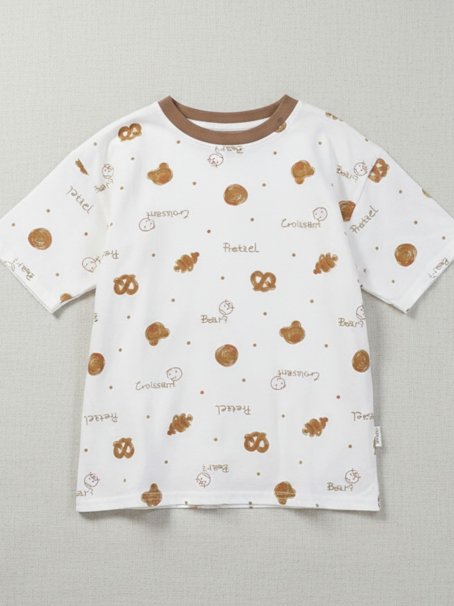 Children's white short-sleeve t-shirt with a brown crew neck, featuring a tossed print of pretzels, croissants, and bear faces with "Pretzel" and "Croissant" text.