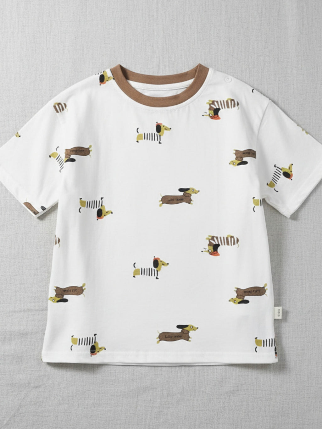 Children's white short-sleeve t-shirt featuring an all-over print of illustrated dachshund dogs in sweaters and hats with a brown crew neck.