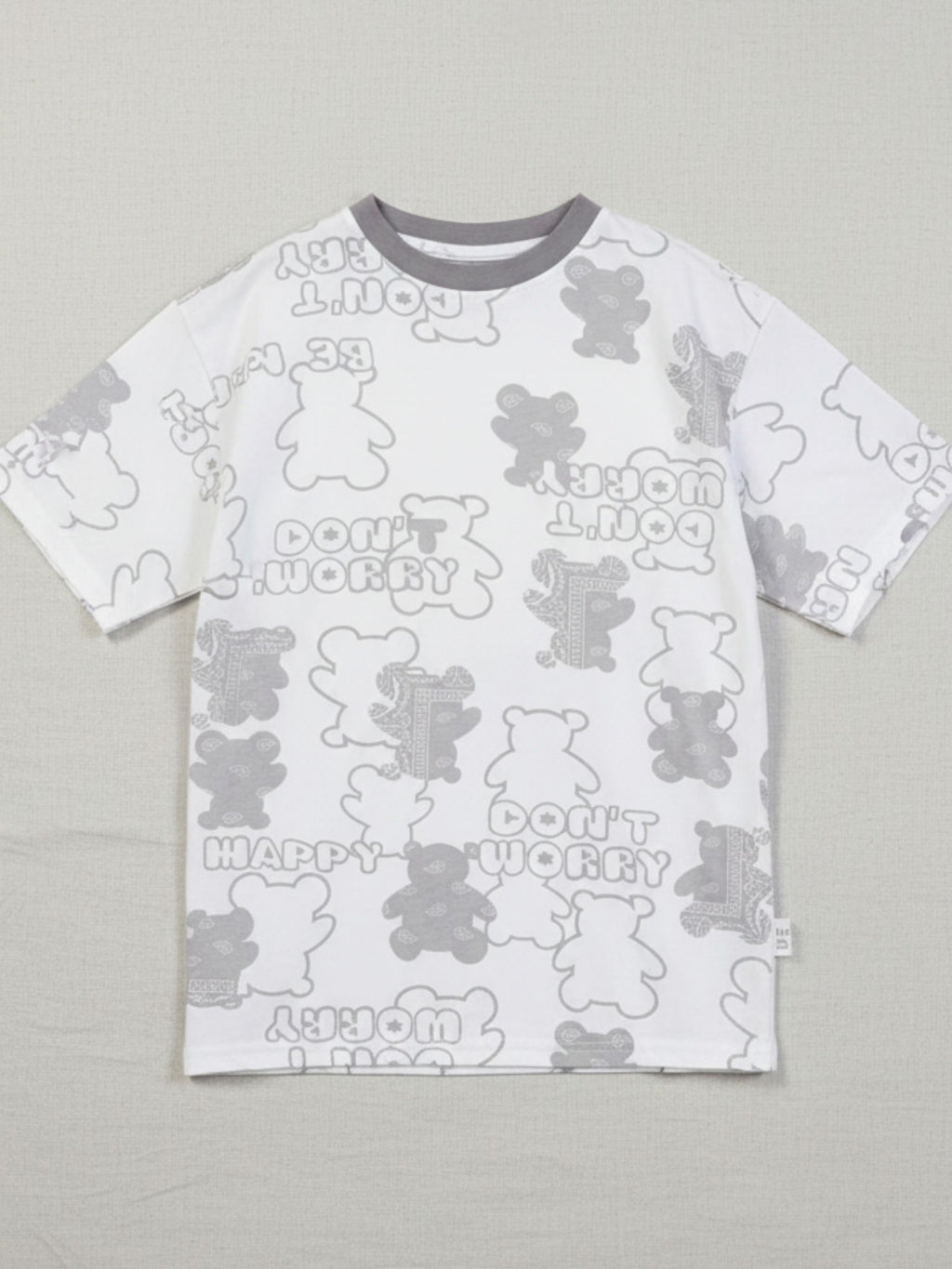 Children's white short-sleeve oversized t-shirt featuring an all-over grey bear silhouette print with "Don't Worry Be Happy" text and a charcoal grey crew neck.