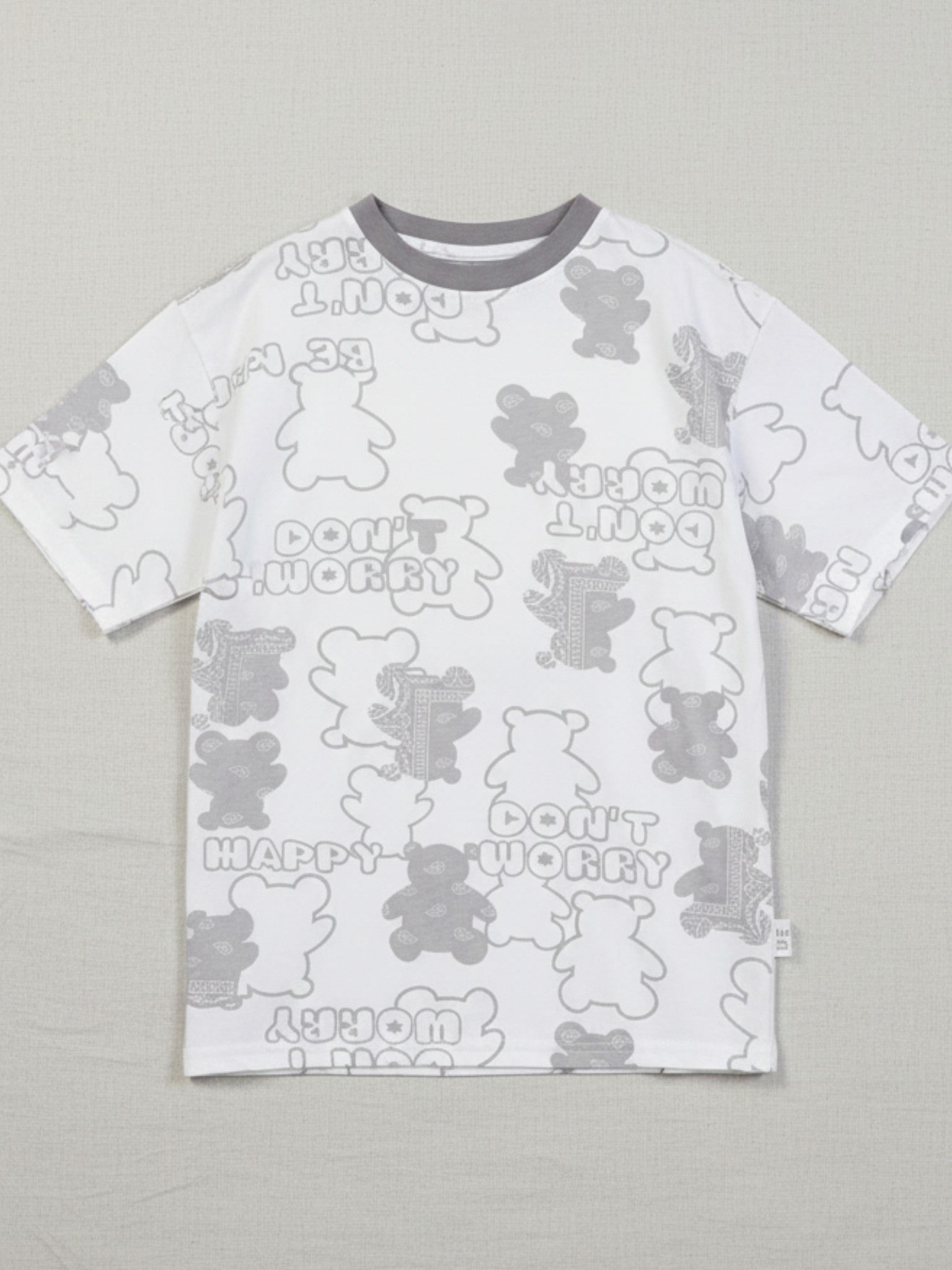 Children's white short-sleeve oversized t-shirt featuring an all-over grey bear silhouette print with "Don't Worry Be Happy" text and a charcoal grey crew neck.