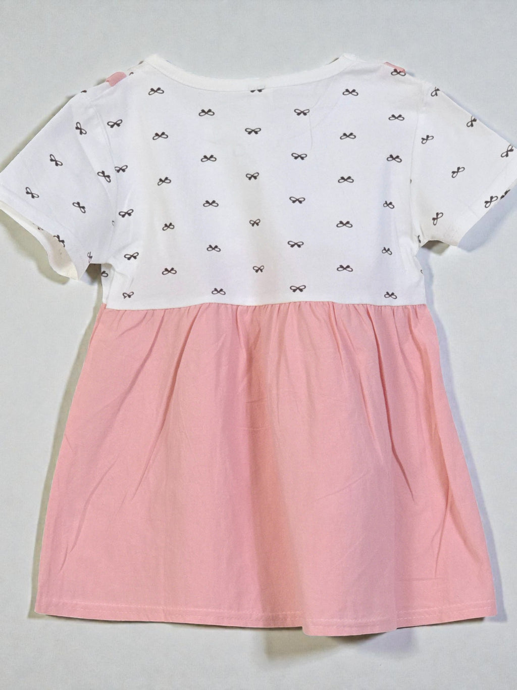 White top with black bow pattern and pink skirt on a light gray background. Pink 1