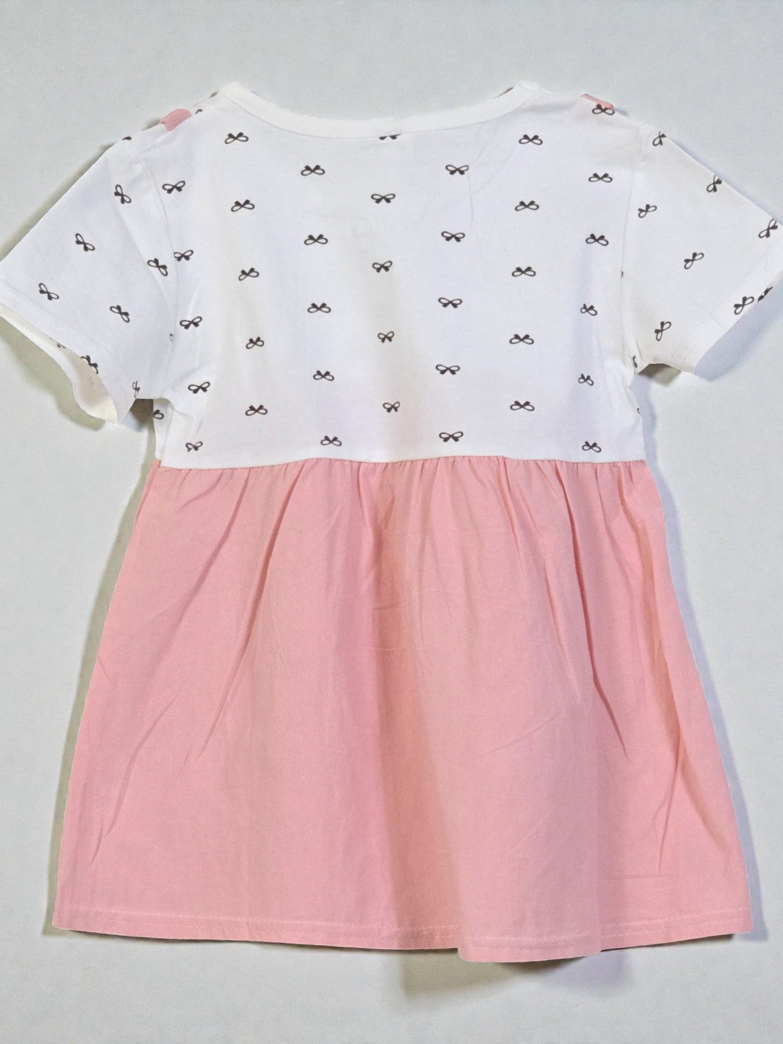 White top with black bow pattern and pink skirt on a light gray background. Pink 1