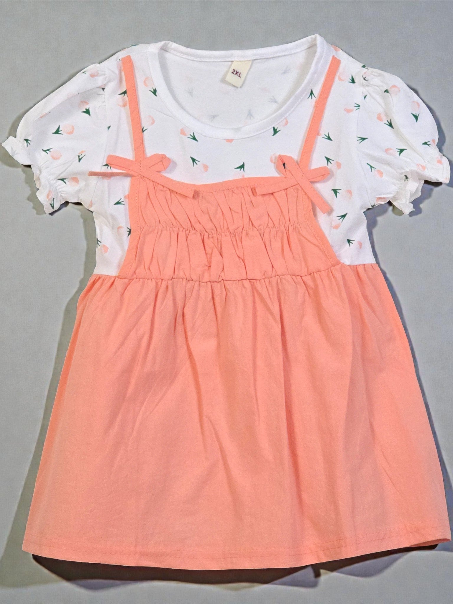 Children's dress with white top and peach-colored skirt on a gray background. Peach