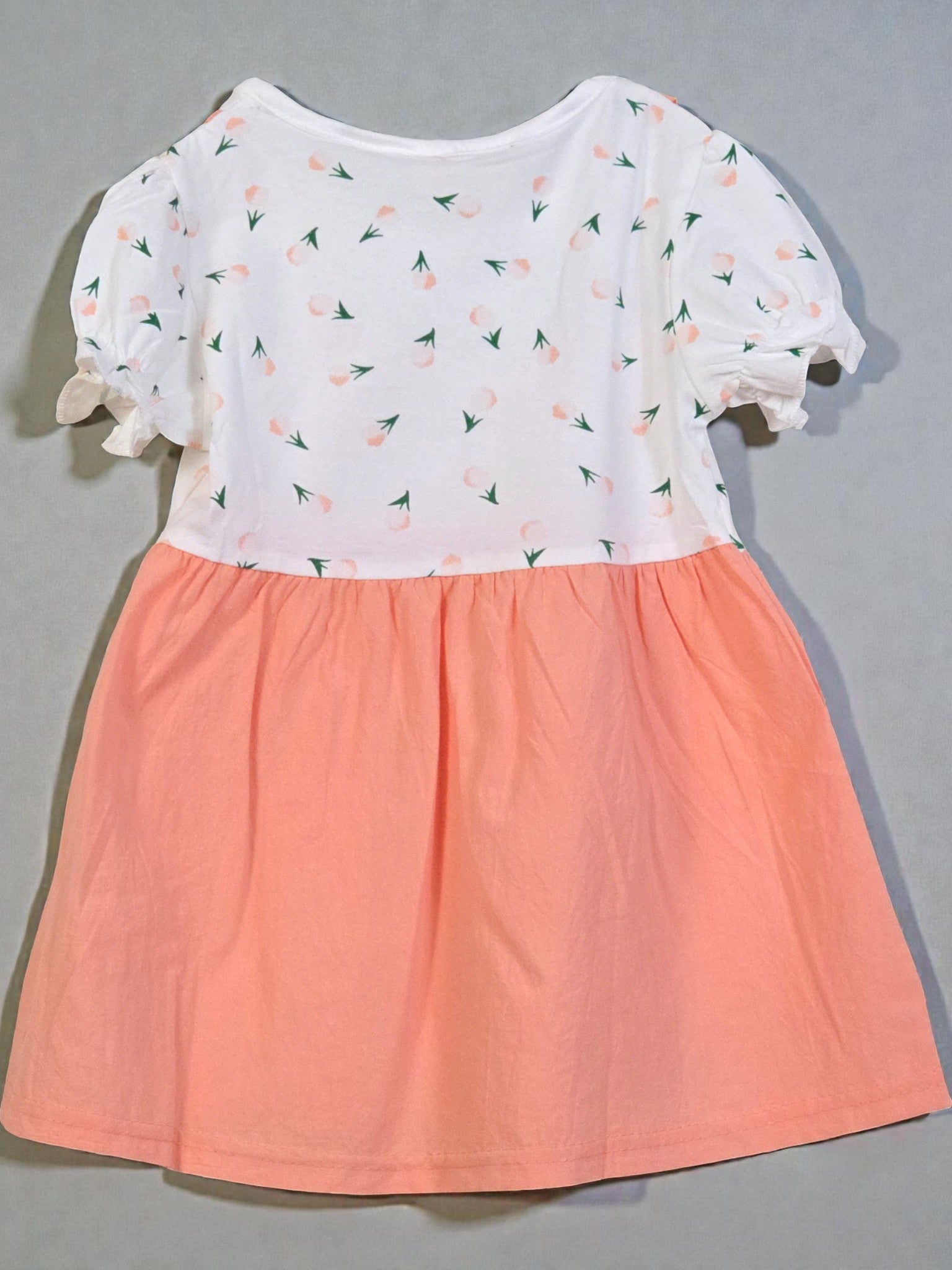Children's dress with white top and peach-colored skirt on a gray background. Peach