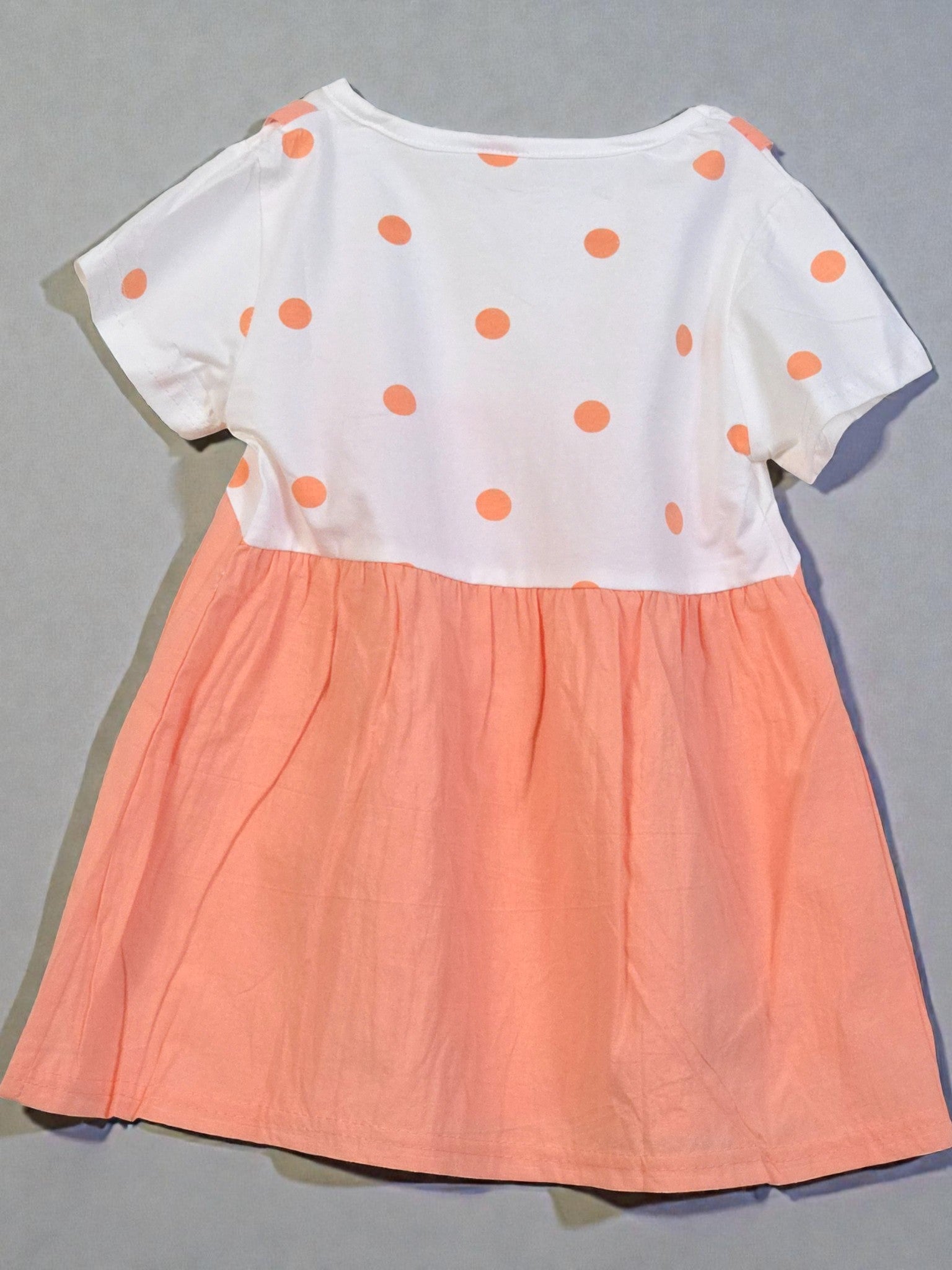 Peach-colored dress with white polka dots and bird design on a gray background. Apricot