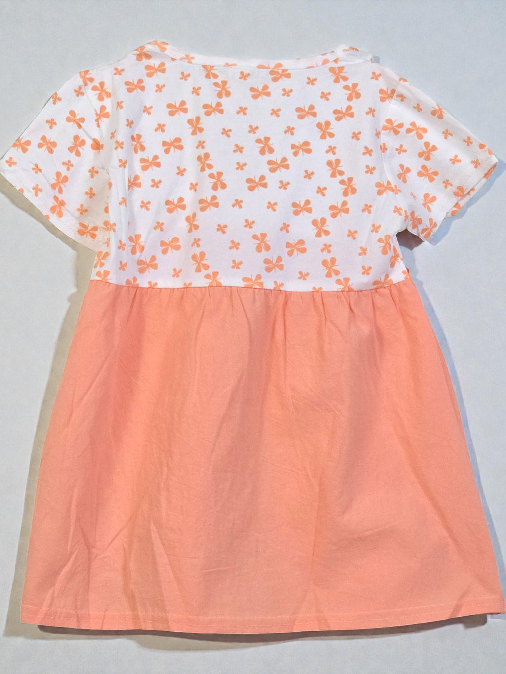 Peach-colored dress with lace details and a white floral top on a light gray background. Pumpkin