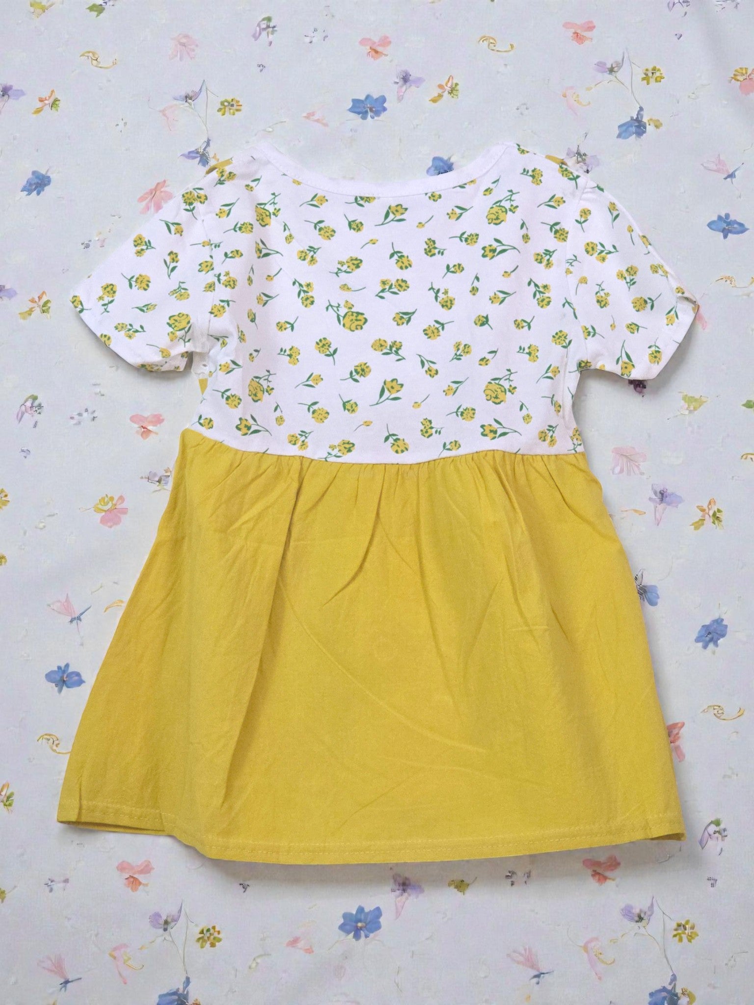 Yellow dress with a white floral top on a light gray background. Daisy
