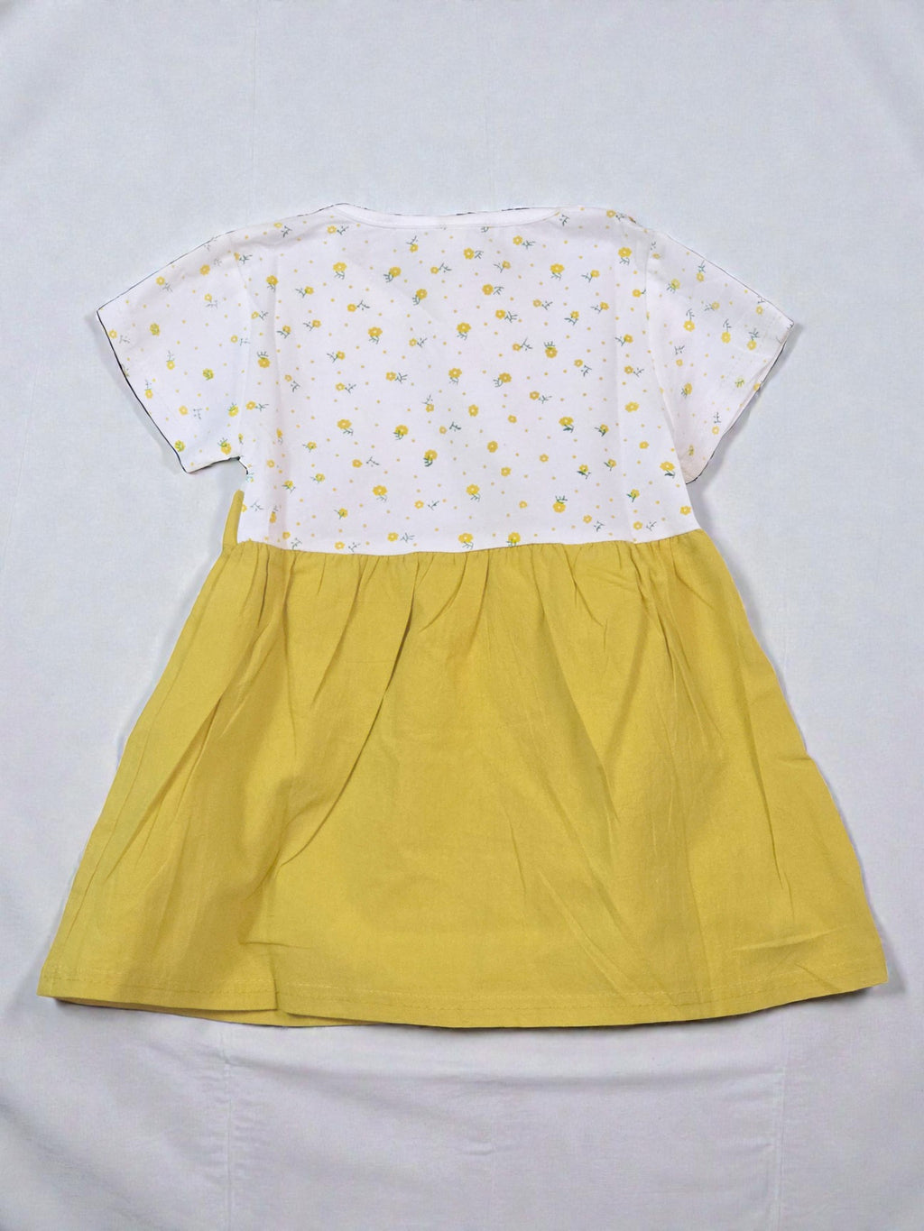 Yellow dress with a white top featuring floral patterns on a tiled background. Sunflower
