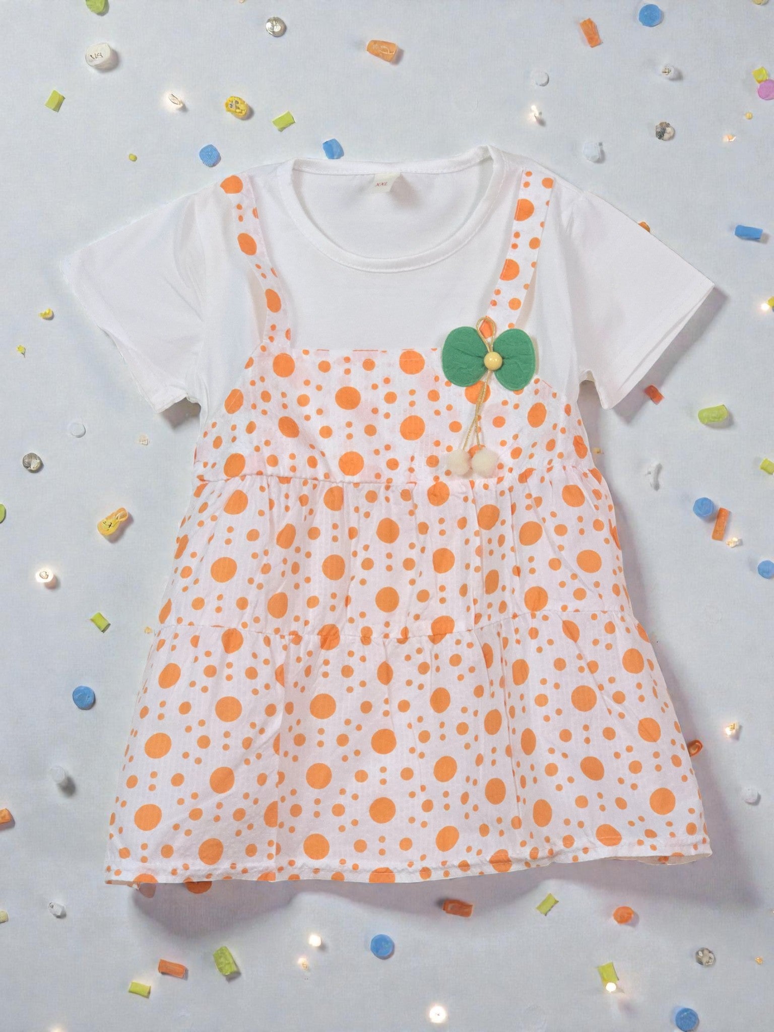 Children's outfit with polka dot dress over a white shirt on a light gray background. Orange