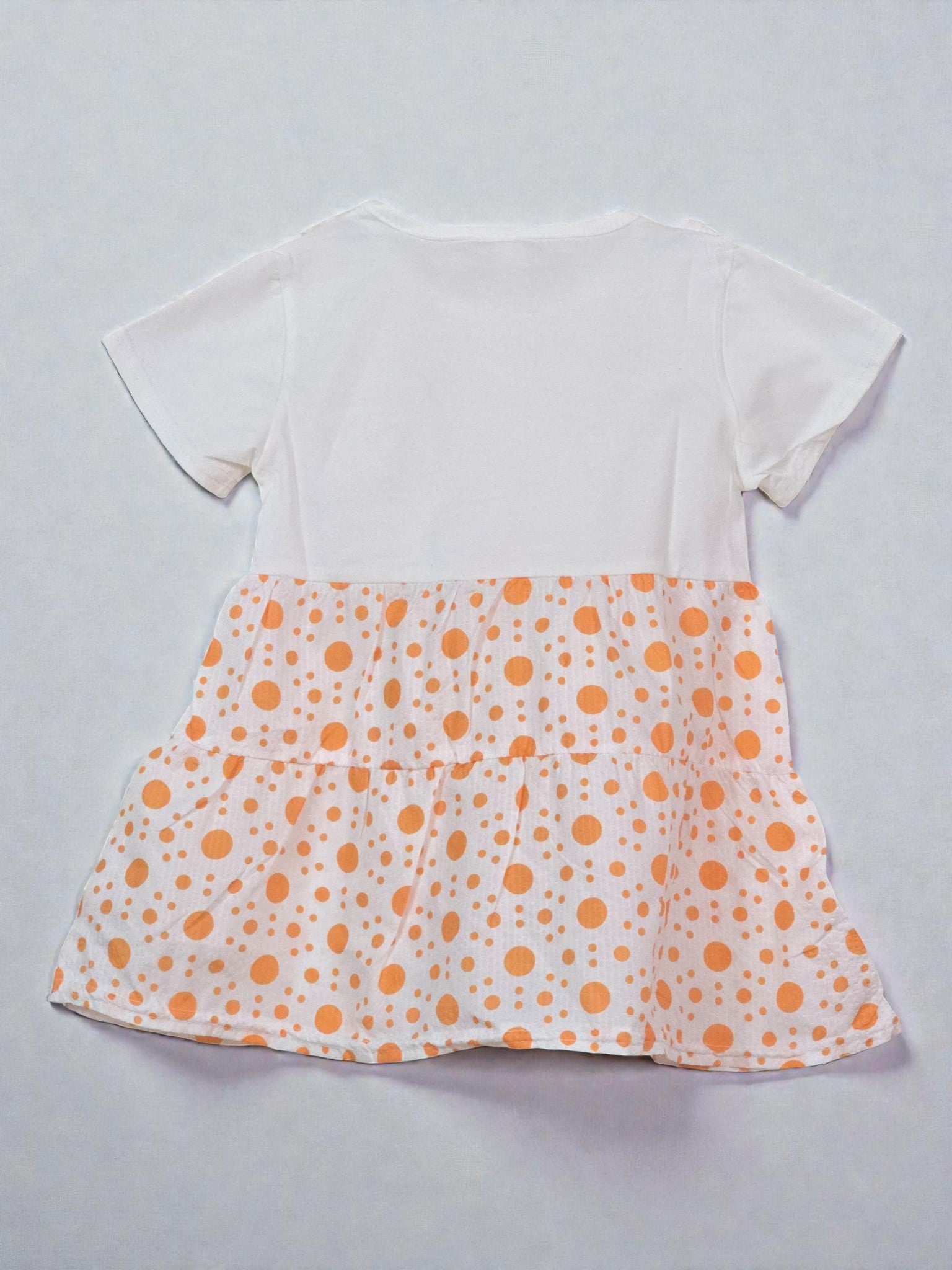 Children's outfit with polka dot dress over a white shirt on a light gray background. Orange
