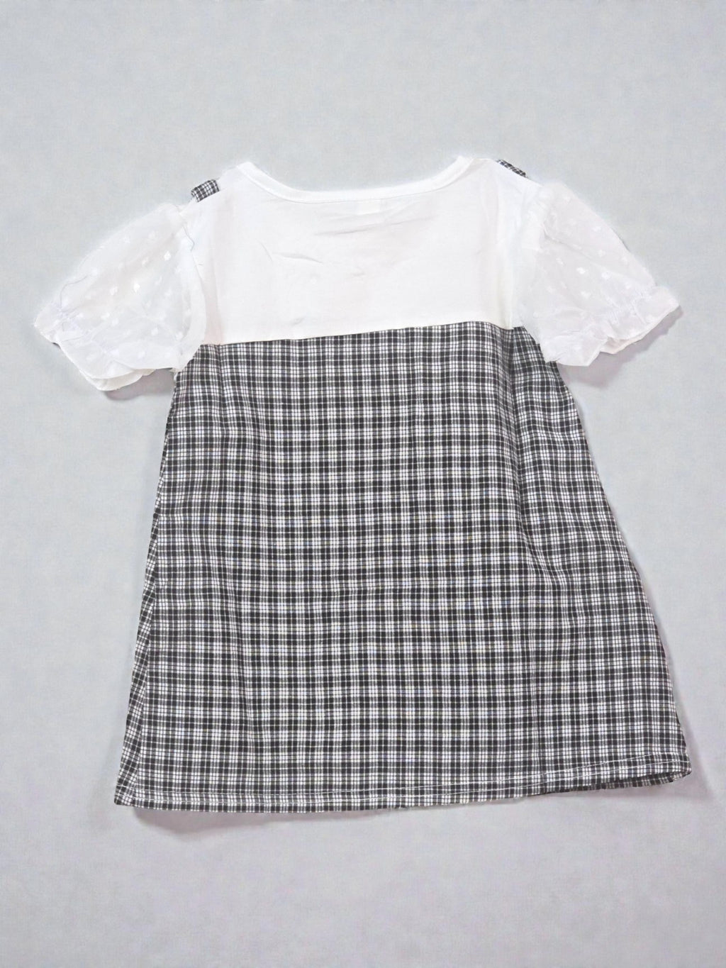 White top with lace details and plaid skirt on a light gray background. Checkered