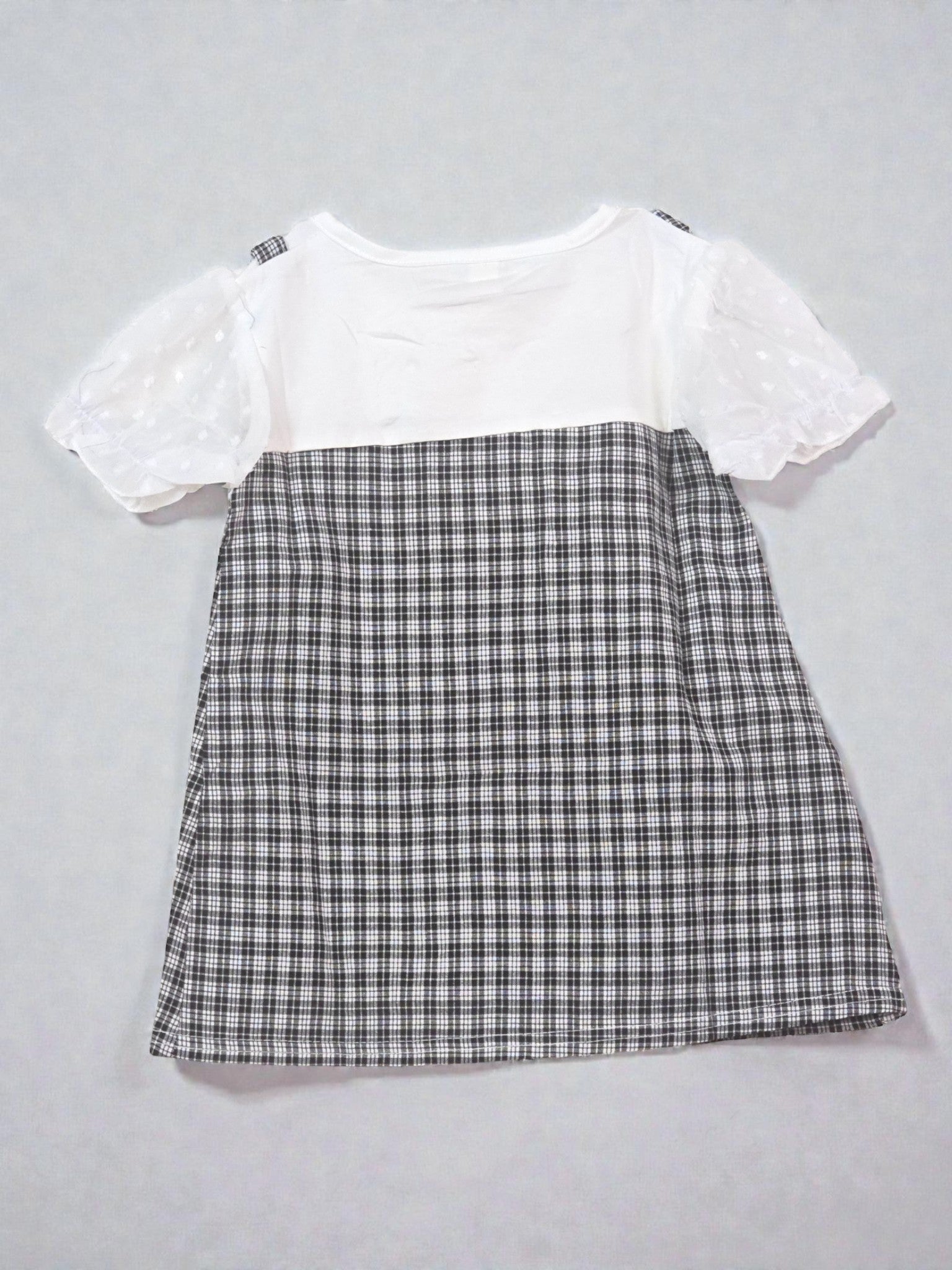 White top with lace details and plaid skirt on a light gray background. Checkered