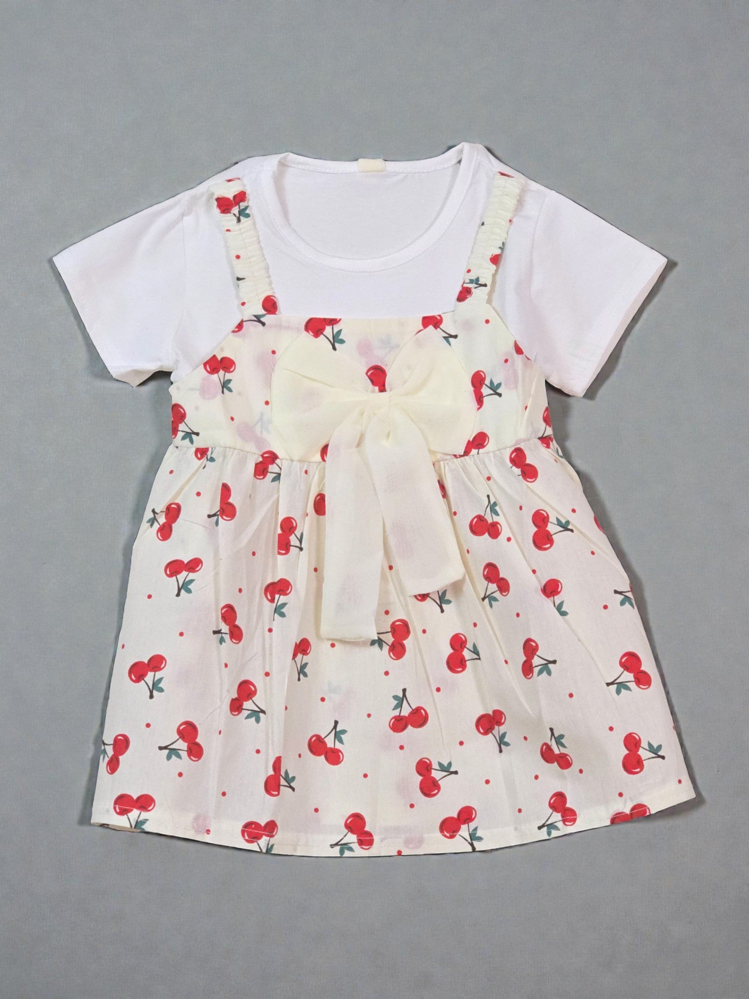 White t-shirt with a cherry-patterned dress over it on a gray background. Cherry