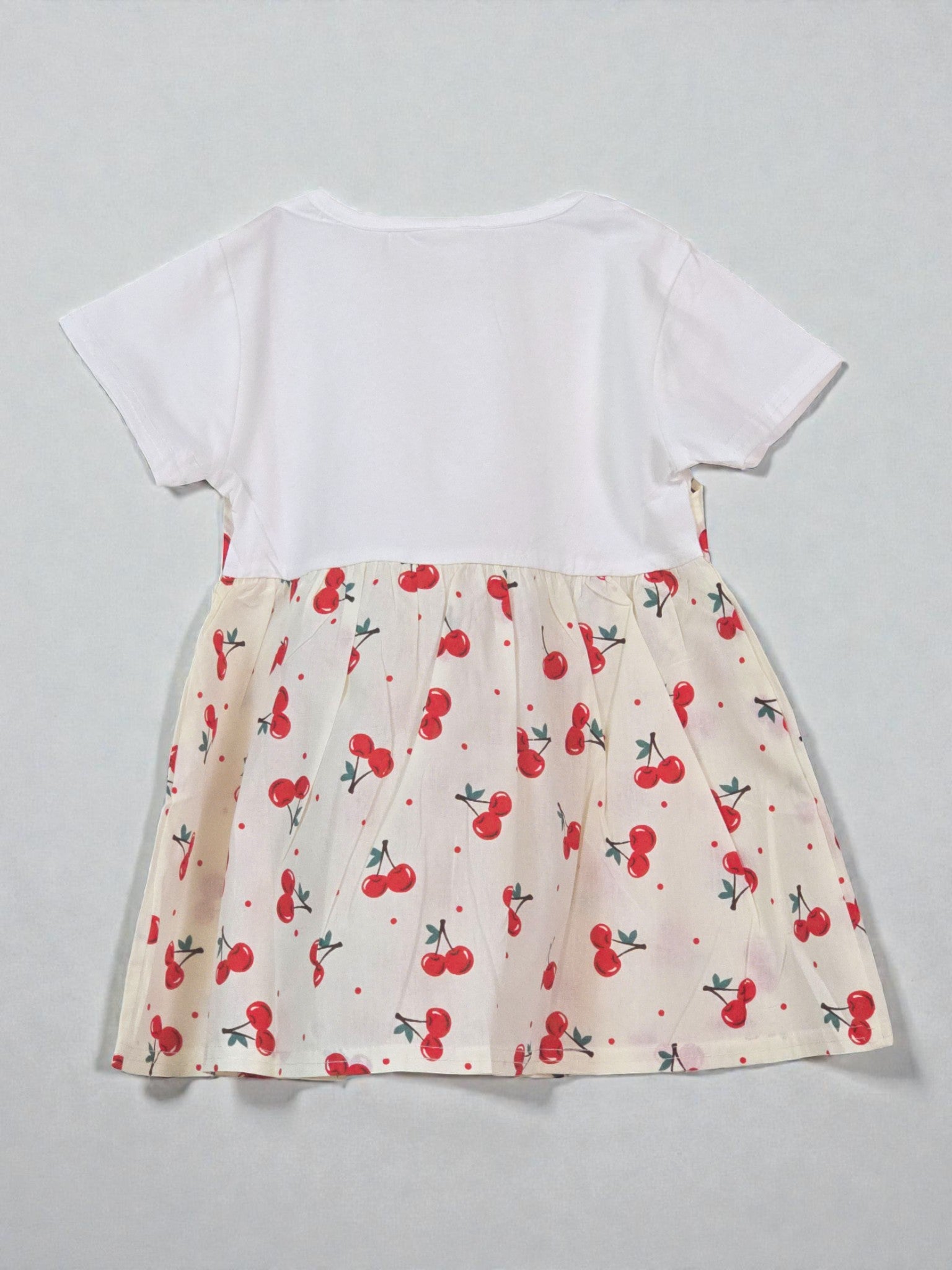 White top with a cream skirt featuring red cherry pattern on a light gray background. Cherry