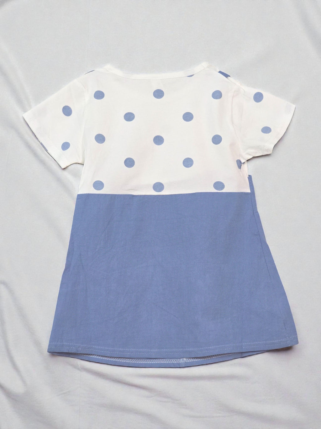 White t-shirt with blue polka dots and a blue bottom section on a gray background Navy