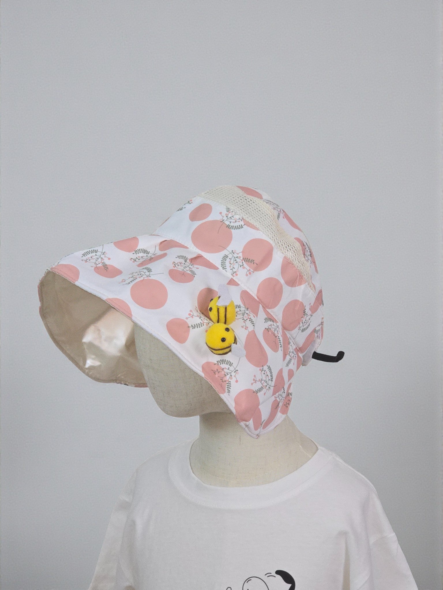 Pink polka dot bucket hat with a yellow character on a mannequin against a white background. Pink