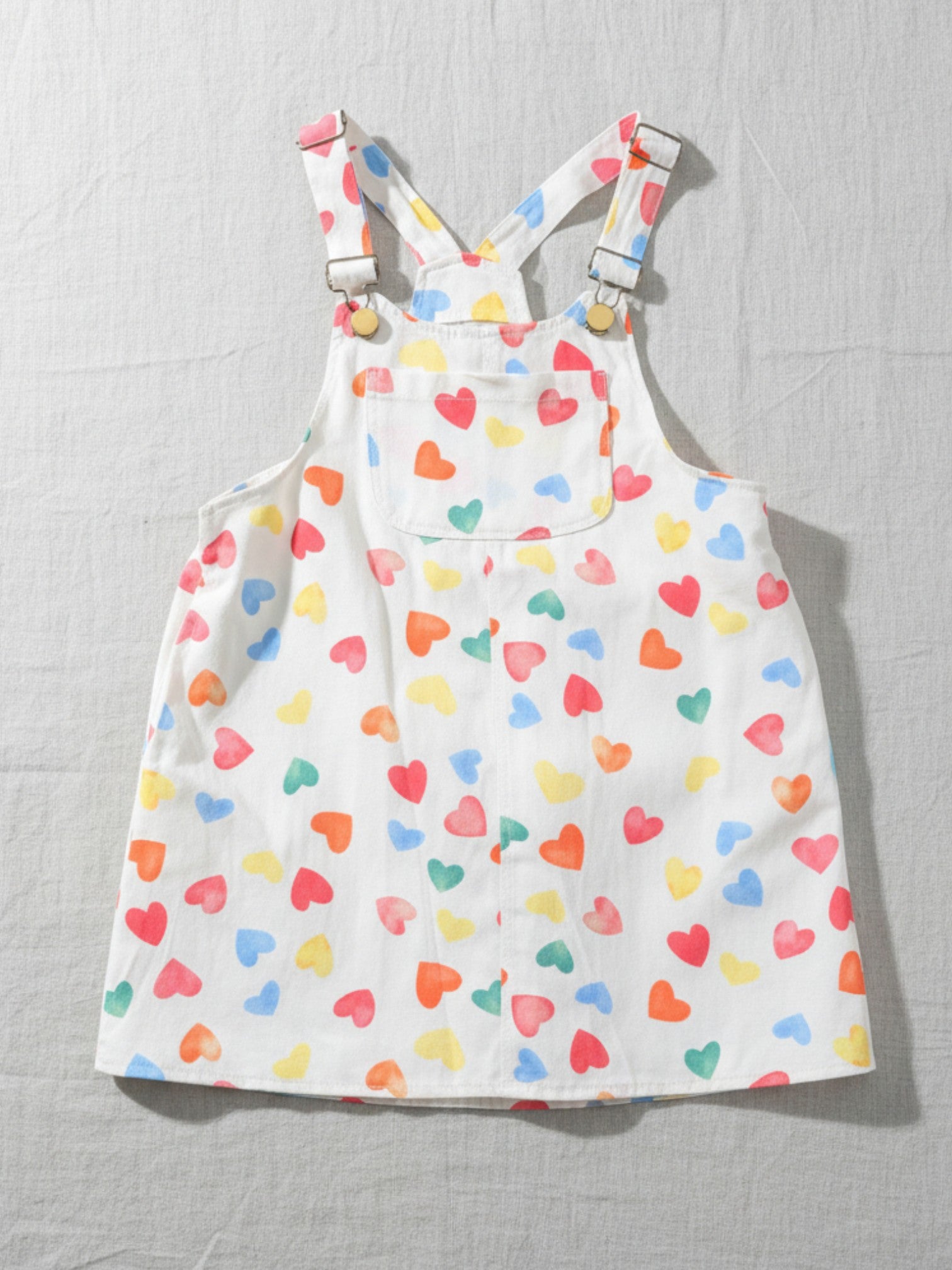 white kids' overalls dress with colorful heart print, versatile and durable cotton fabric for stylish and comfortable play.