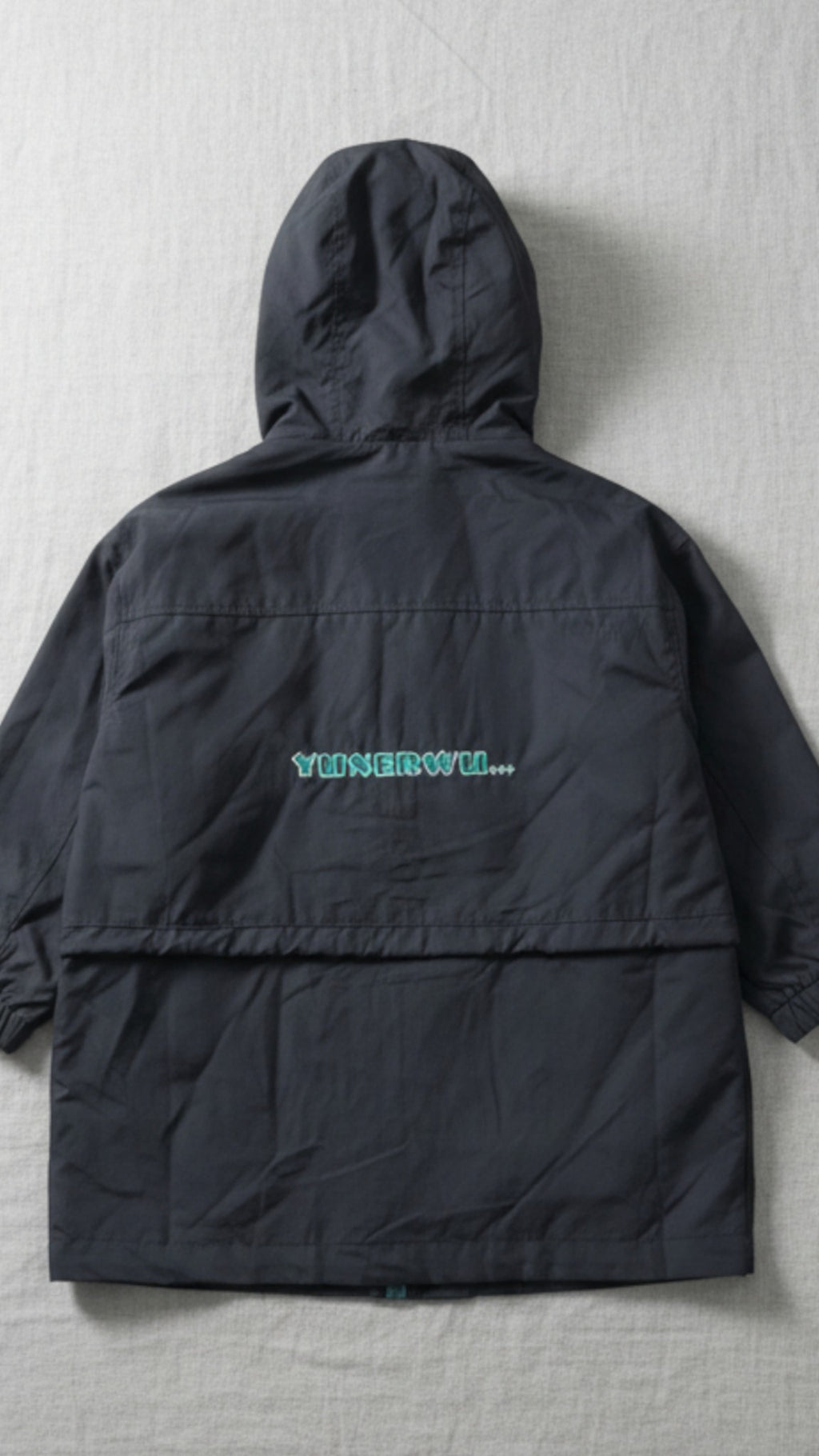 Kids black hooded parka jacket featuring a teal graphic on the chest, adjustable drawstrings, and elasticated cuffs