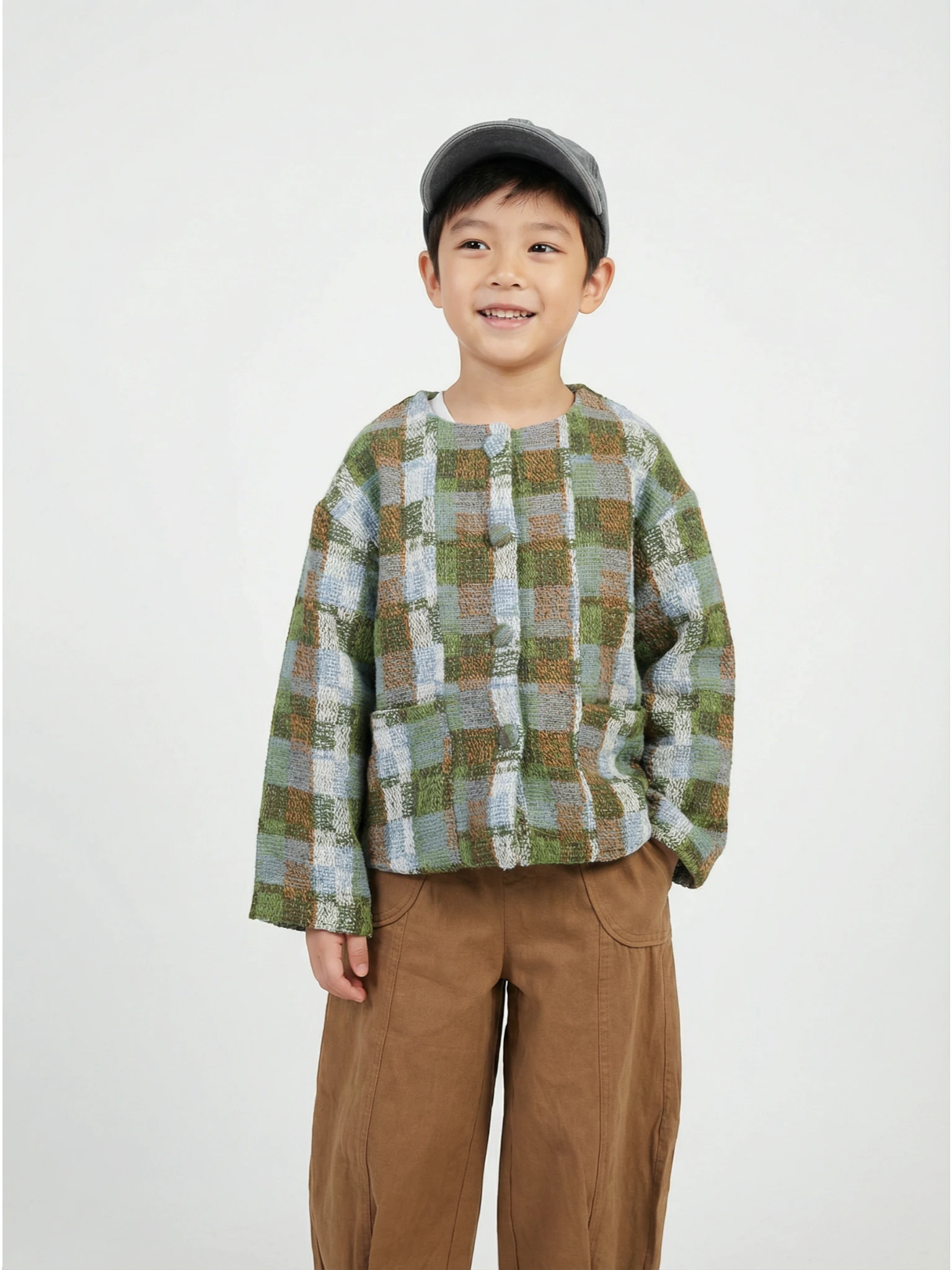 Boy wearing a thick, textured plaid jacket in green, brown, and blue earthy tones with front patch pockets and fabric-covered buttons.