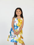 Kids sleeveless white A-line dress featuring a vibrant, oversized abstract botanical and tropical watercolor print in yellow, blue, and ochre.