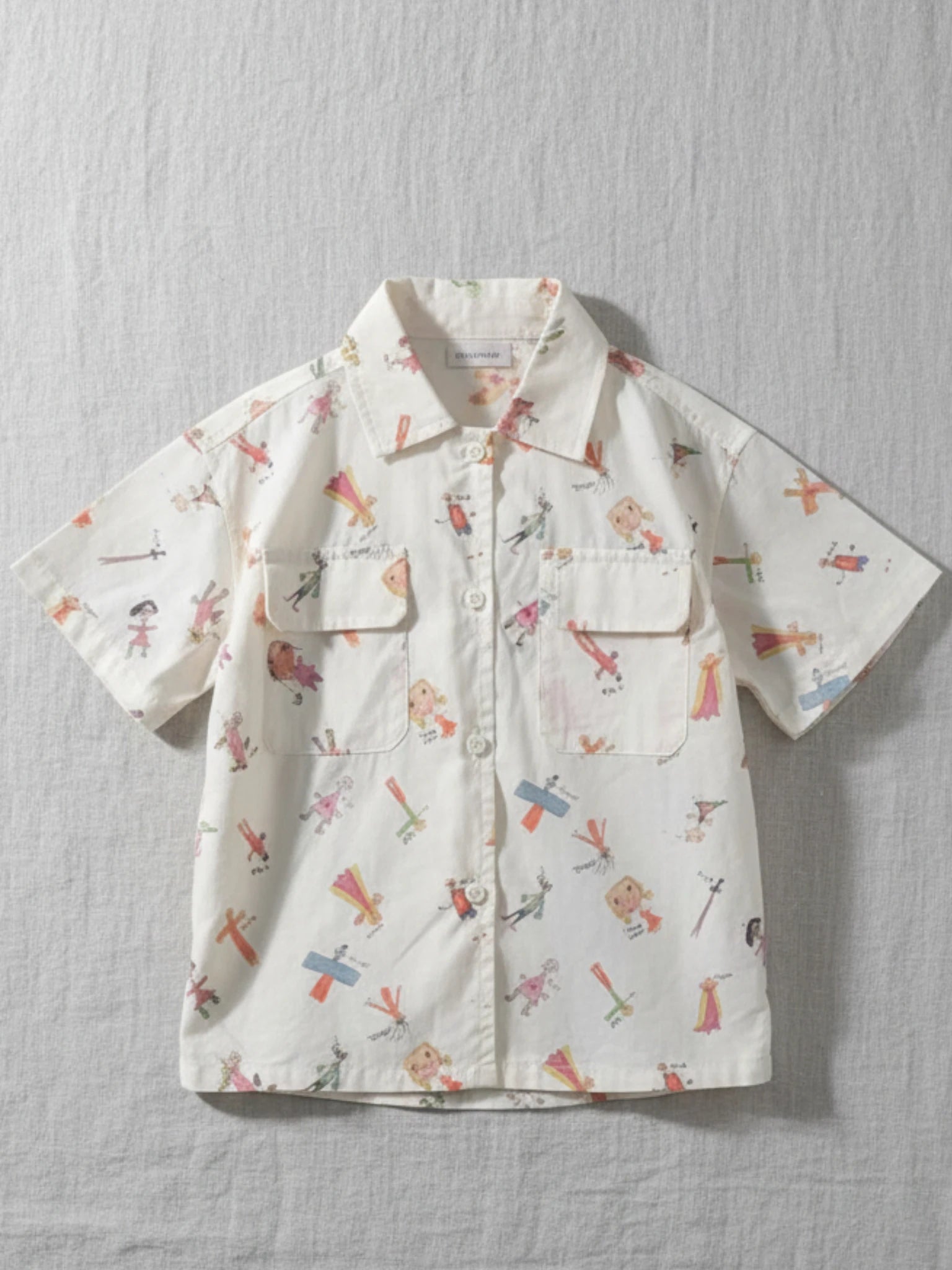 Kids short sleeve button-down shirt featuring an all-over whimsical character doodle print with dual chest pockets