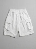 Kids white short-sleeve cargo shorts with an elasticated waistband and large side flap pockets displayed on a neutral textured background.