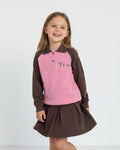 Young girl wearing a brown and pink long-sleeve shirt with 'Yew' printed on it, standing against a white background.