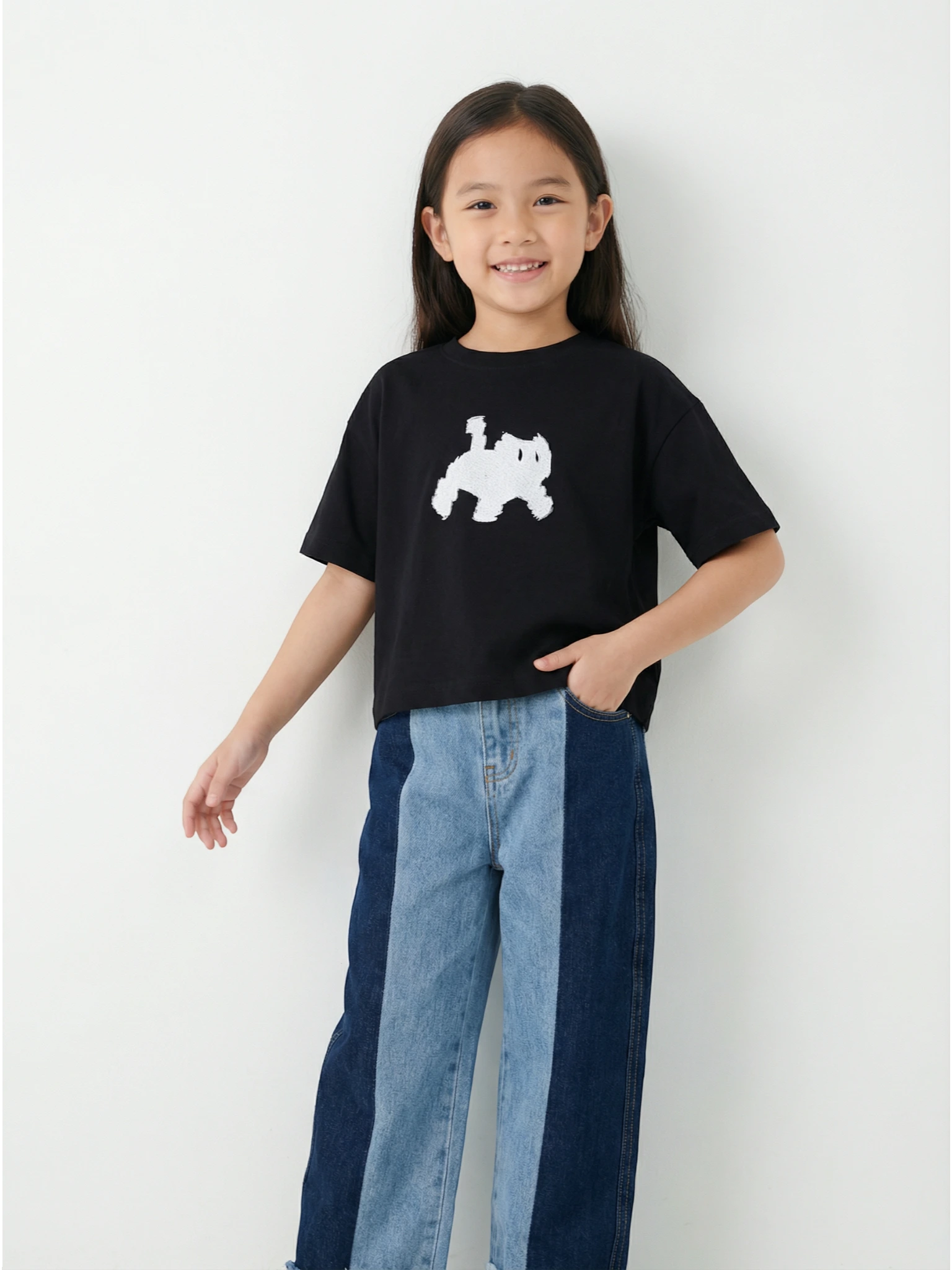 Child wearing a black t-shirt with a white graphic and blue jeans on a white background