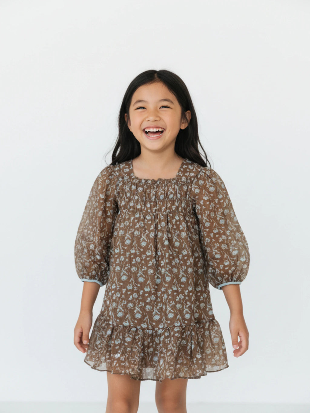 brown floral chiffon dress with a smocked bodice, ¾ balloon sleeves, and a ruffled hem on a white studio background.