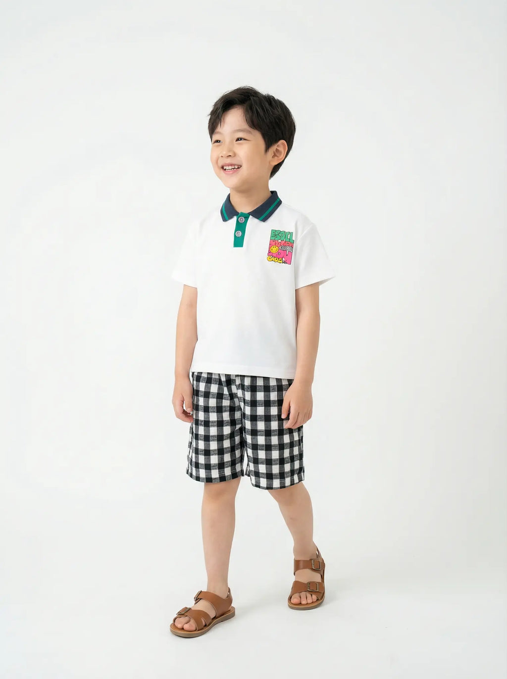Child wearing a white polo shirt with a colorful patch and black checkered shorts on a white background