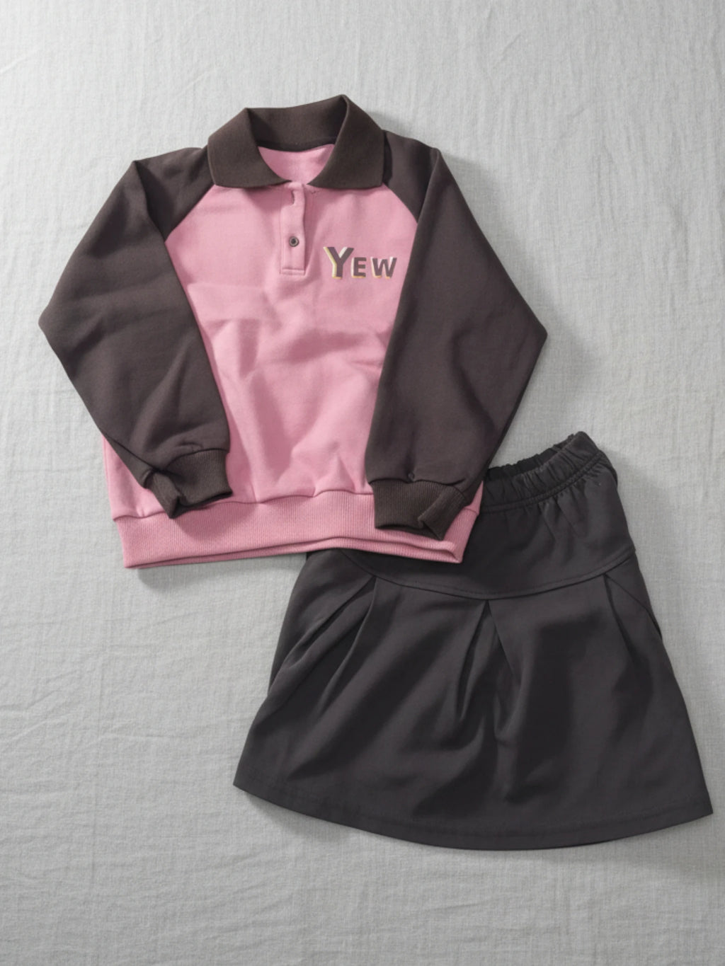 girls Pink sweatshirt with 'YEW' text and brown skirt on a gray background