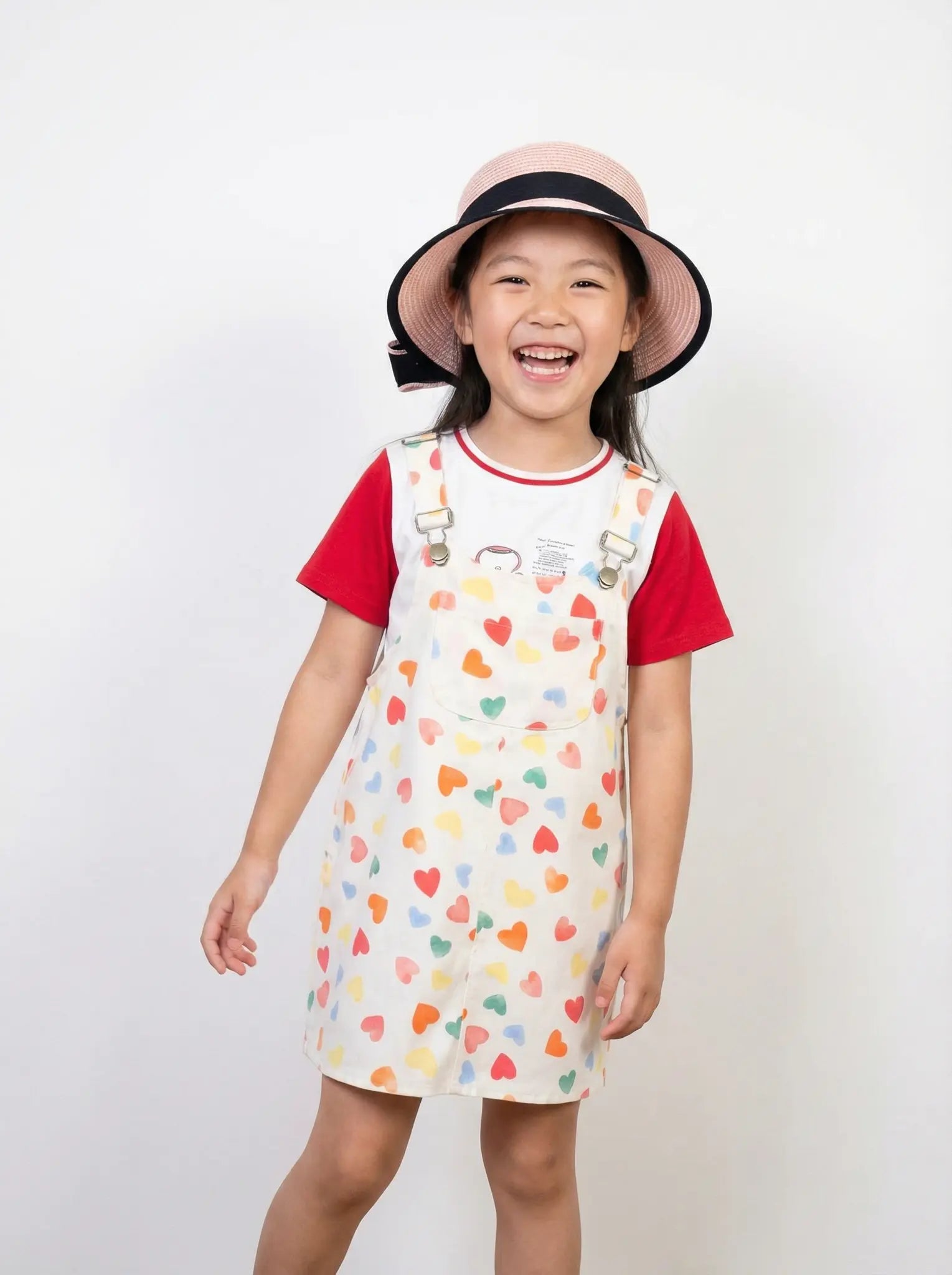 Child wearing a dress with colorful heart pattern and red sleeves, standing against a plain background